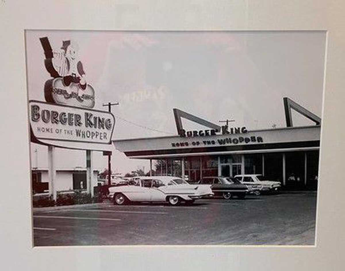 Black-and-white photo of a vintage Burger King restaurant, one of the notable companies founded by year, with a large "Burger King Home of the Whopper" sign and classic cars parked outside.