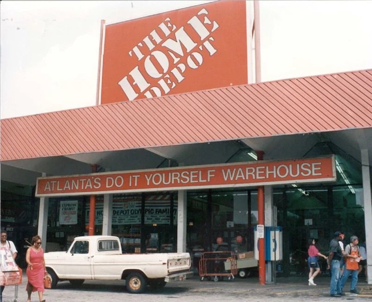 A vintage photo of a Home Depot store—one of the iconic companies founded by year 1978—shows a large red sign above the entrance, “THE HOME DEPOT,” and another below reading, “ATLANTA'S DO IT YOURSELF WAREHOUSE.” People and an old pickup are outside.