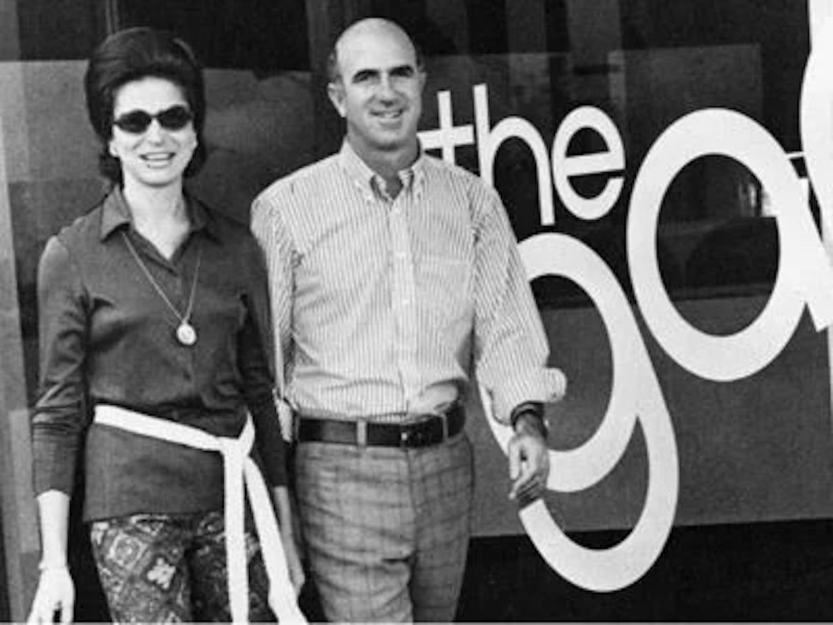 A woman and a man stand smiling in front of a building with large letters spelling "the gap," one of the companies founded by year in 1969. The image is black and white, with both dressed in casual 1960s or 1970s clothing.