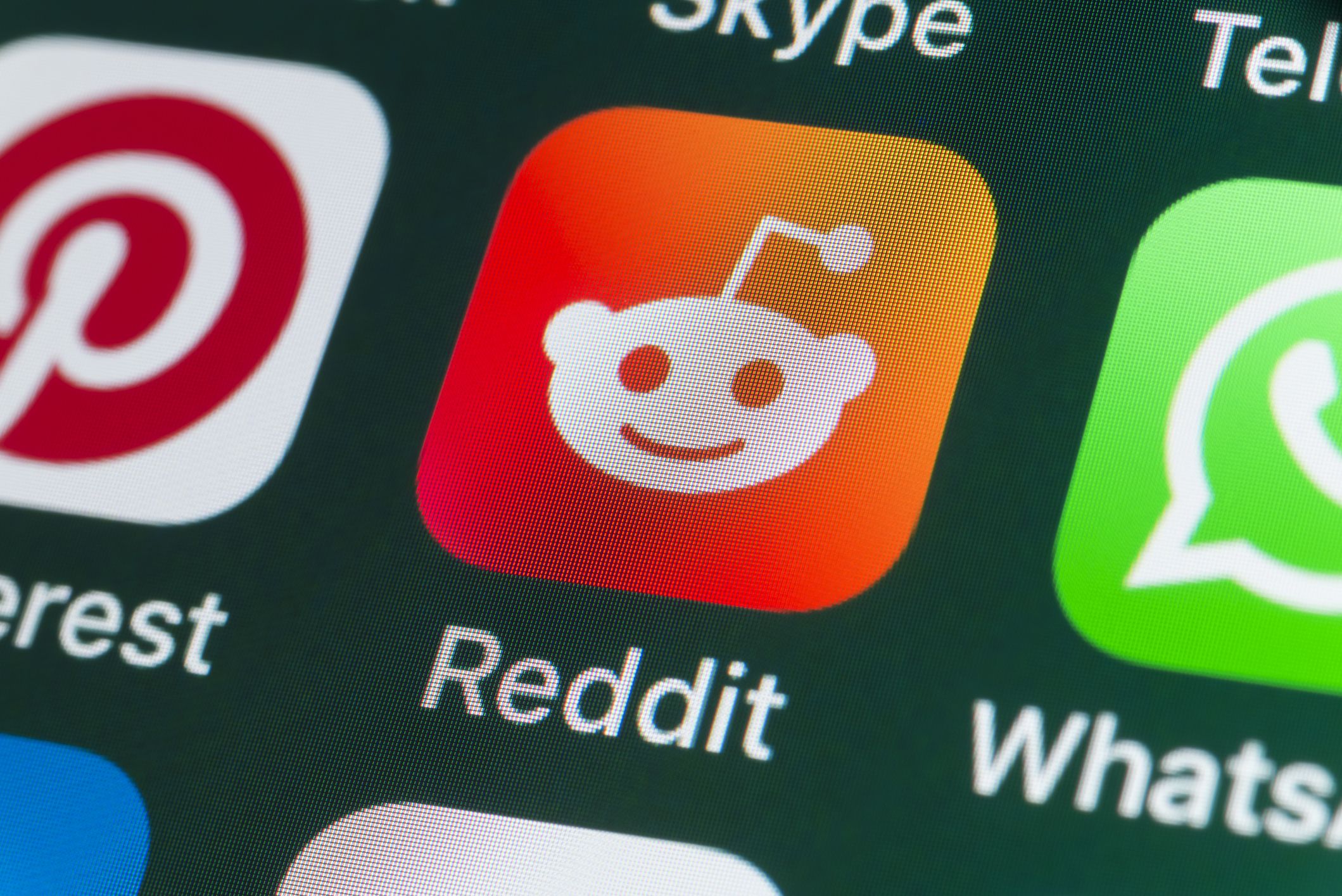 London, UK - July 31, 2018: The buttons of the app Reddit, surrounded by Pinterest, Whatsapp, and other apps on the screen of an iPhone.