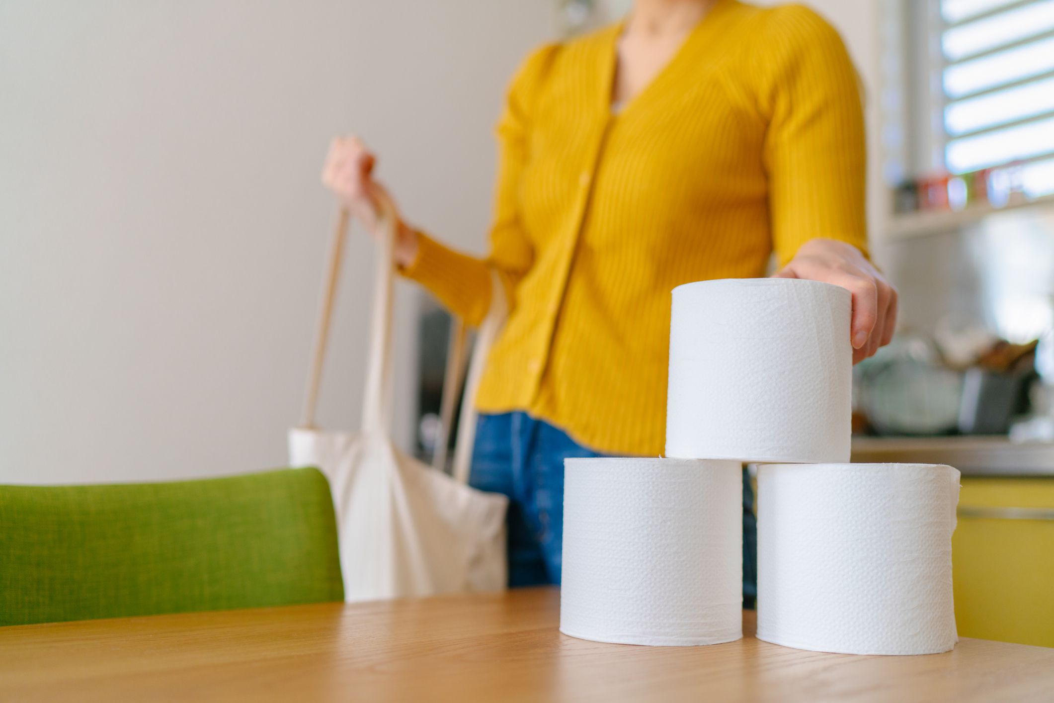 A young woman is taking out toilet papers from a reusable shopping bag at home.