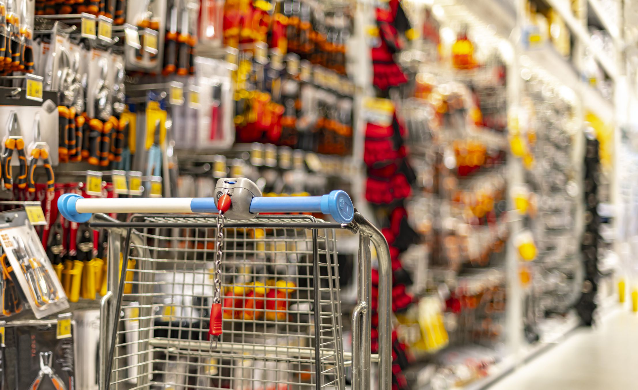 A shopping cart by a store shelf in a hardware store.