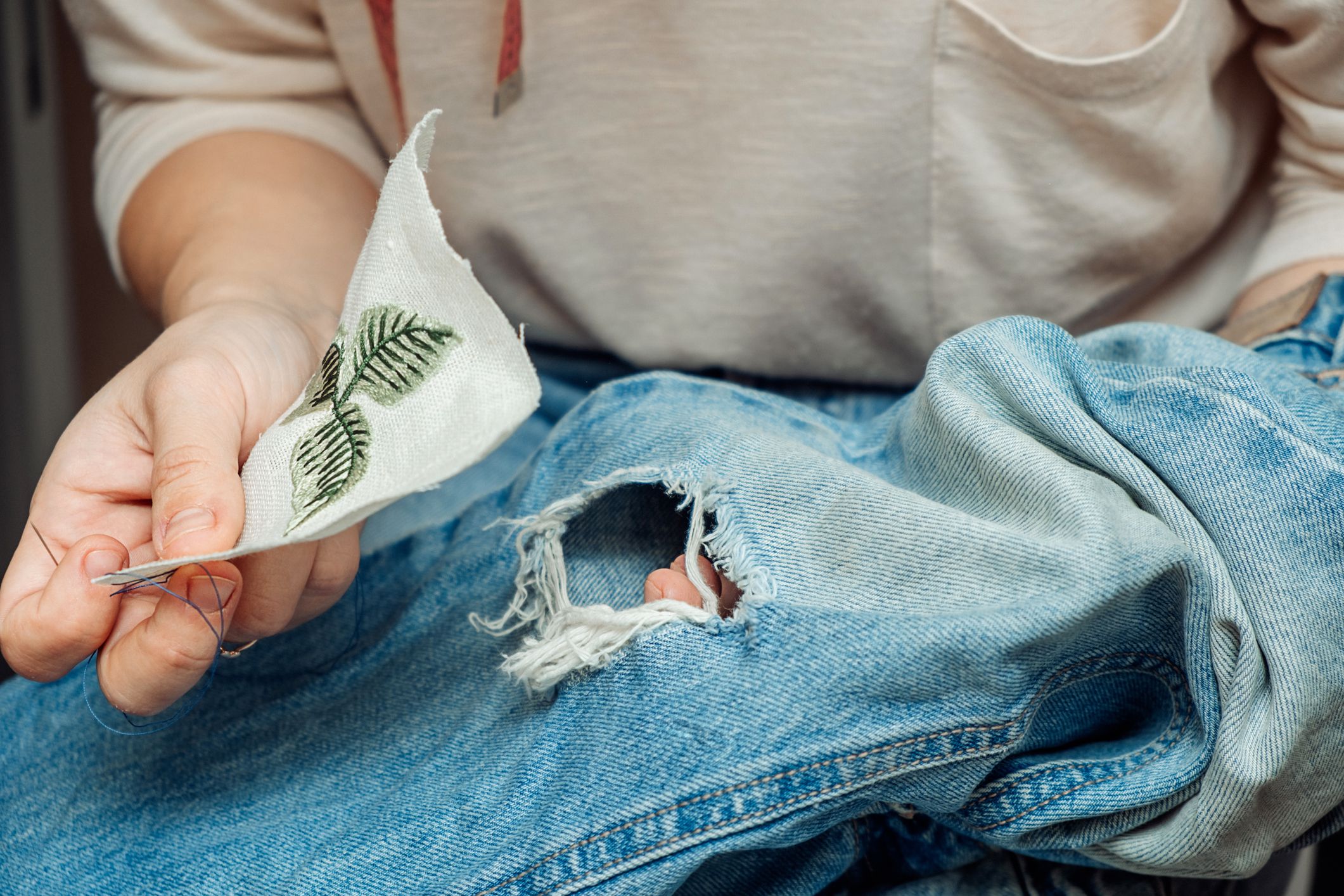 A woman mends jeans, sews a patch on a hole, hands close-up.Mending clothes concept,reusing old jeans.