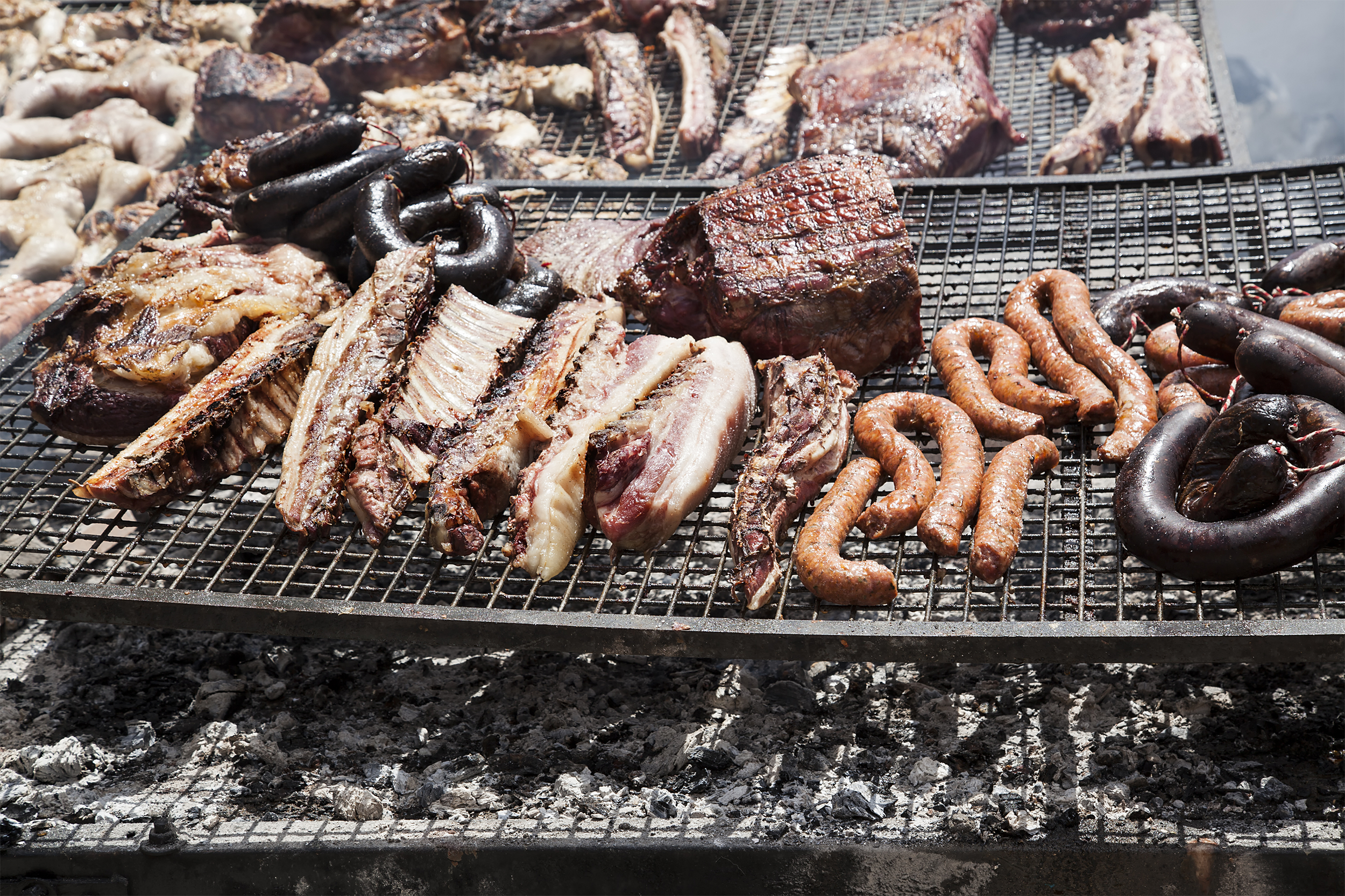 various meats cooking on a grill grate over coals