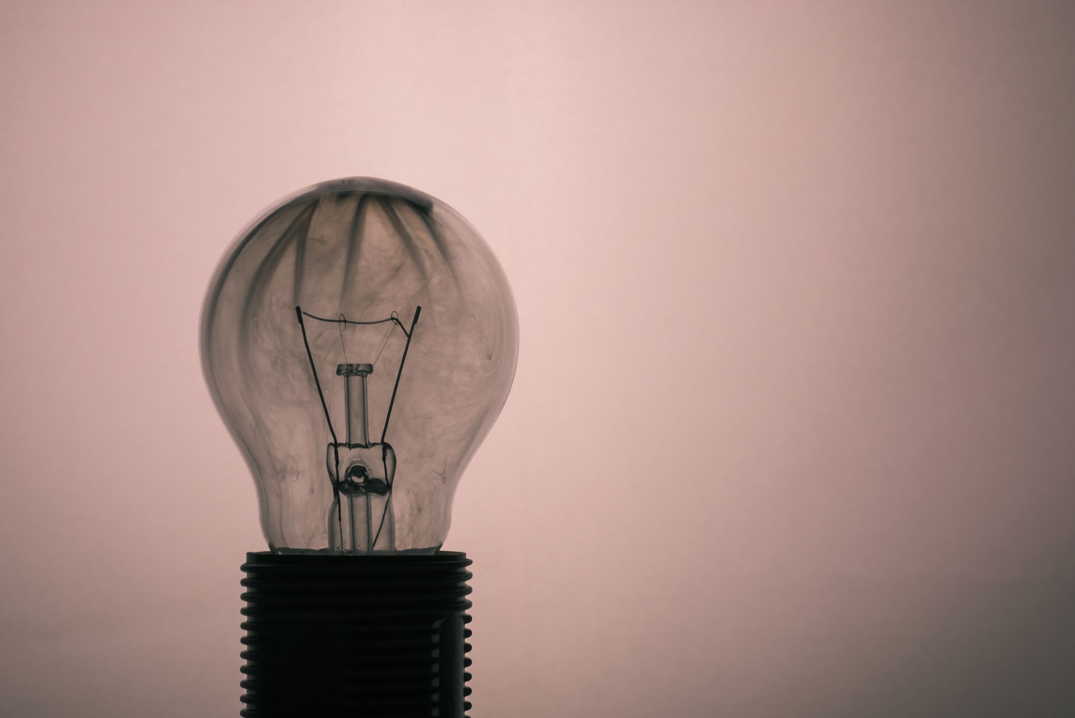 Horizontal photo of single glass bulb placed in the socket on light background. The grey smoke inside was caused by burning wire. The glass is dirty after the flames and fire.