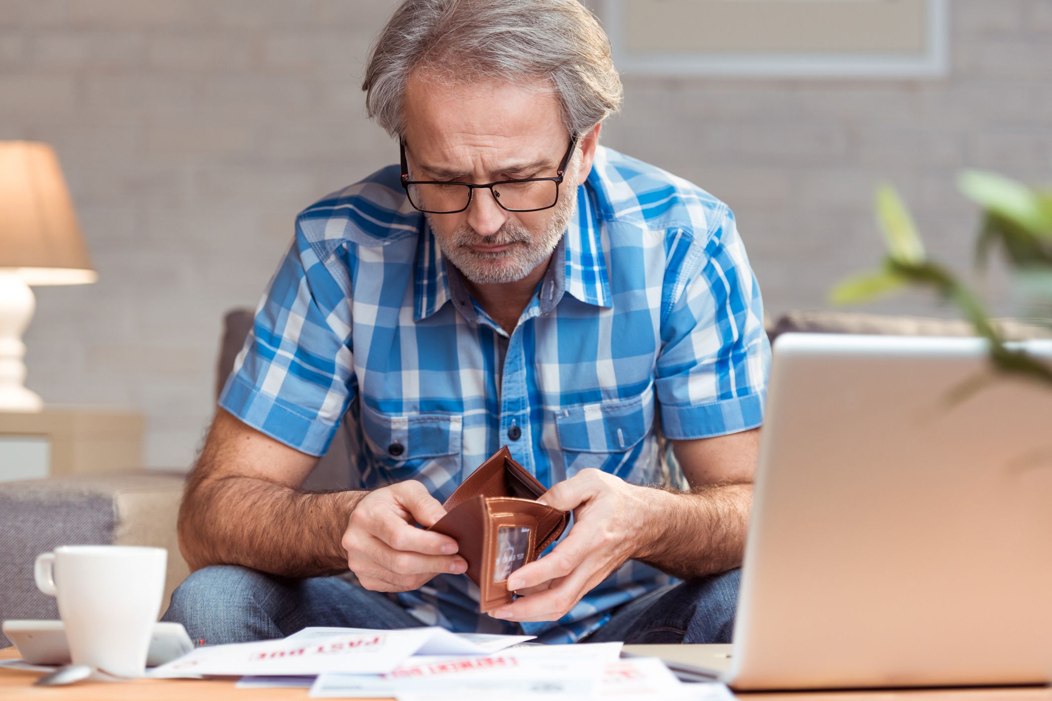 senior man with bills on table, wallet open