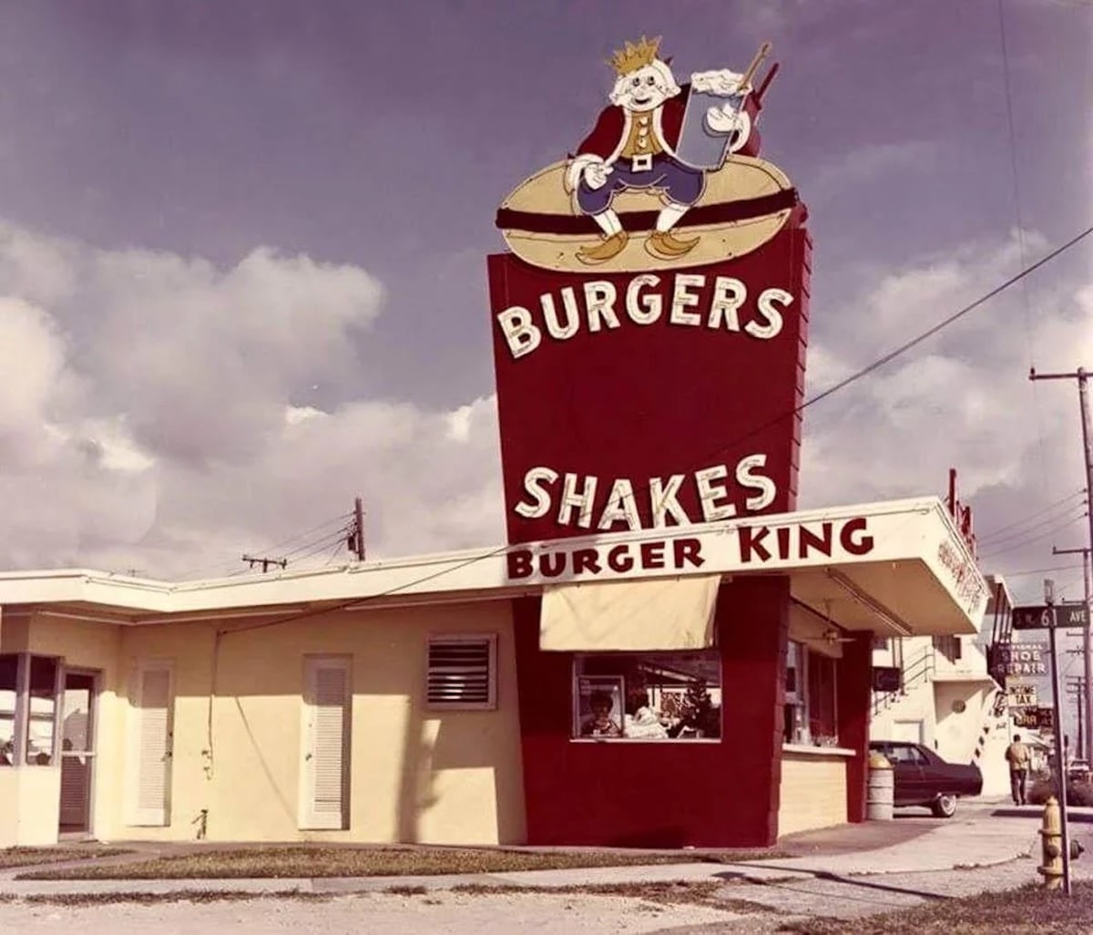 A vintage Burger King restaurant, part of companies founded by year 1954, features a retro design, a large red sign with a cartoon king on a burger, and advertises classic burgers and shakes at its small service window.