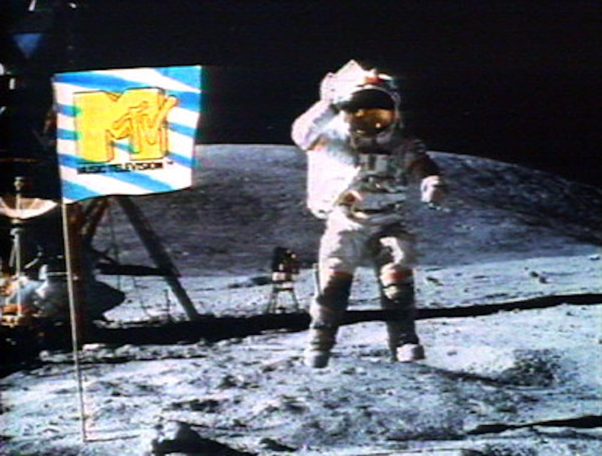 An astronaut in a spacesuit stands on the Moon, saluting near an MTV flag—a nod to iconic companies founded by year. A lunar lander is visible in the background against the dark sky.