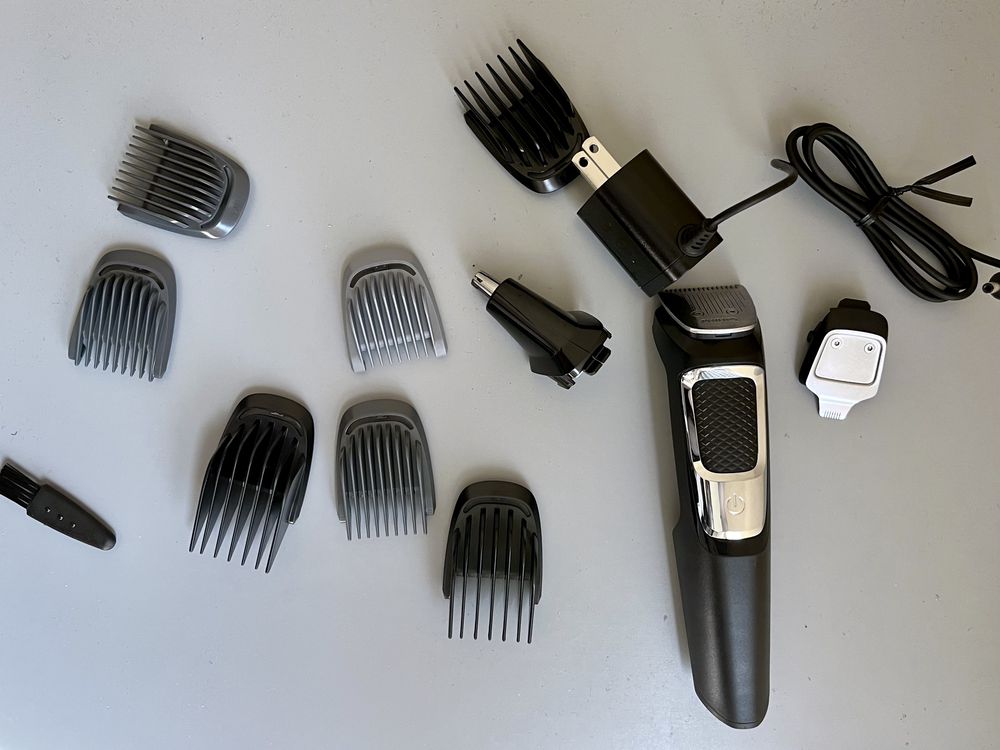 A black electric hair trimmer with multiple clipper guards, attachments, and a charging cord arranged on a gray surface.