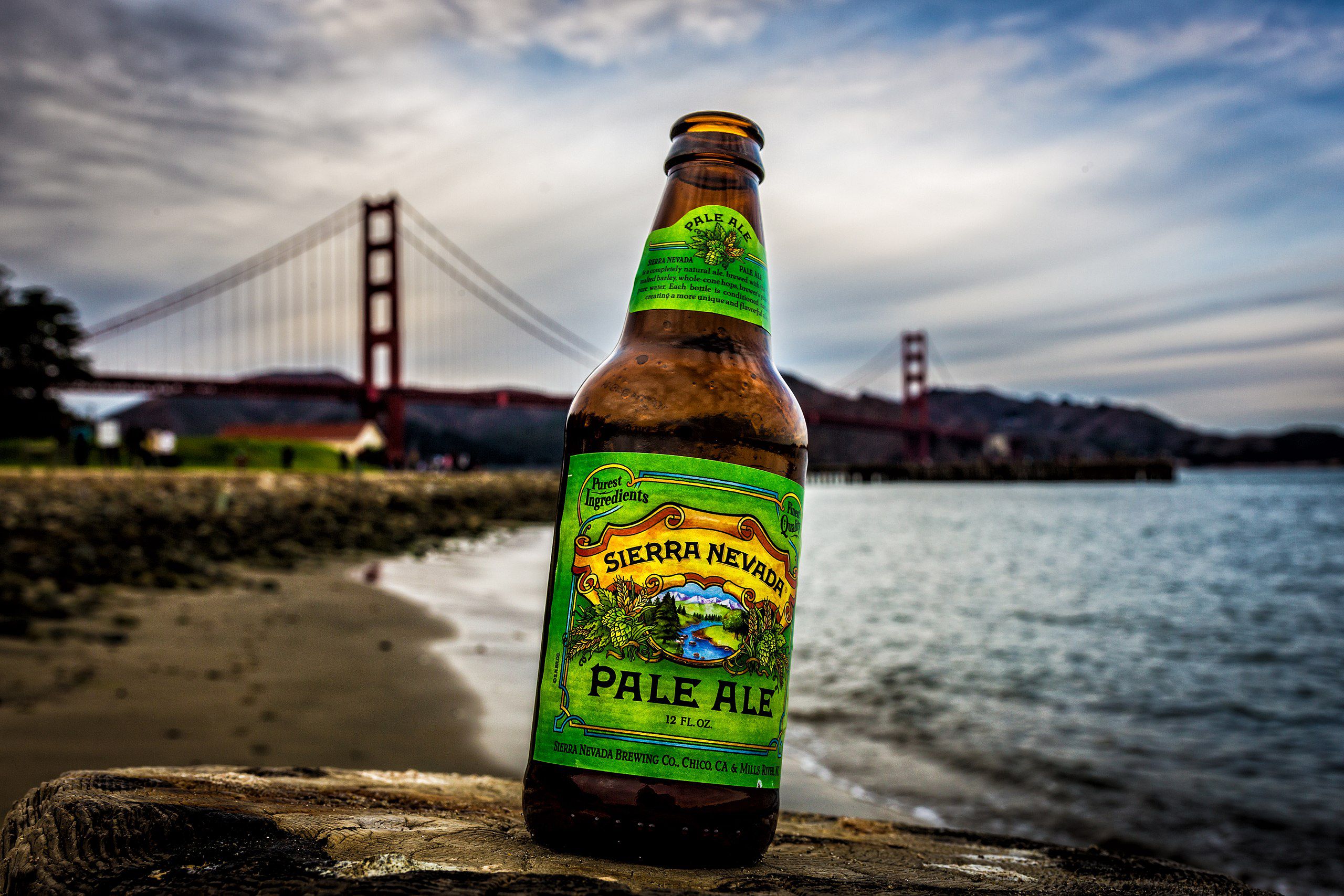 Sierra Nevada - Pale Ale bottle of beer in front of a bridge on a sandy beach