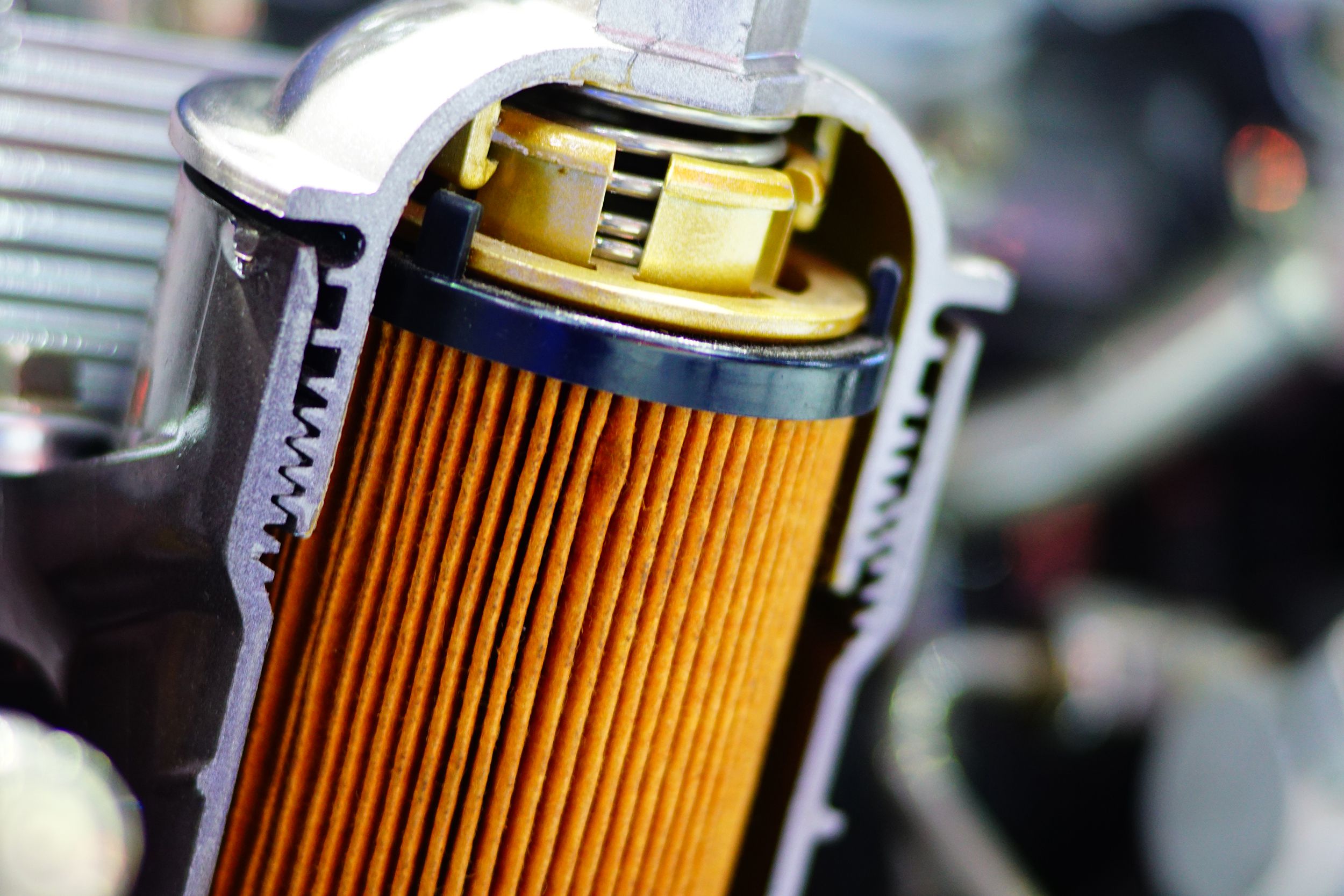 Closeup of a used longitudinal cross section of a car engine oil filter, colored orange, blurred background of car engine