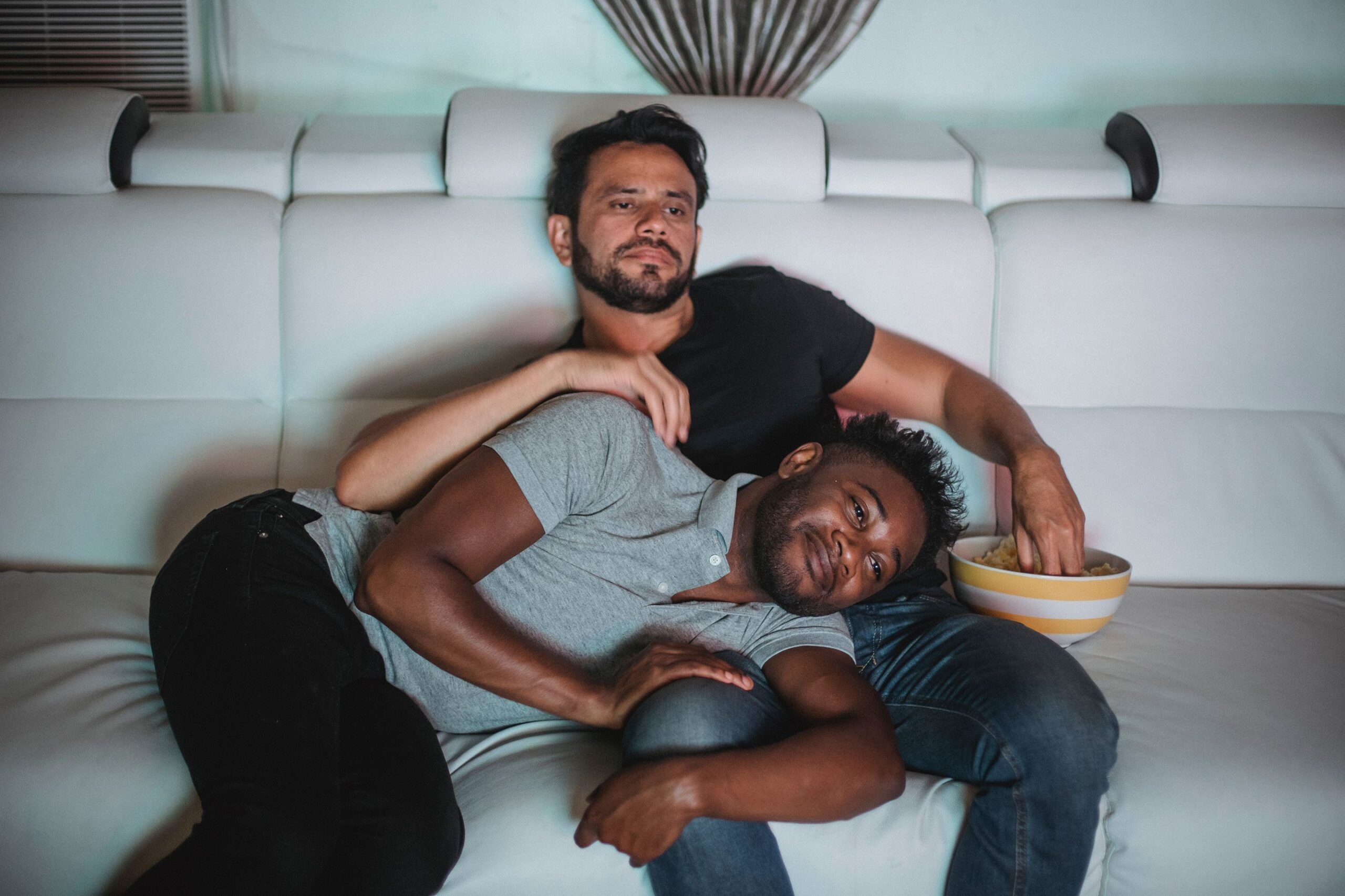 Young couple watching TV and cuddling on the sofa, eating popcorn.
