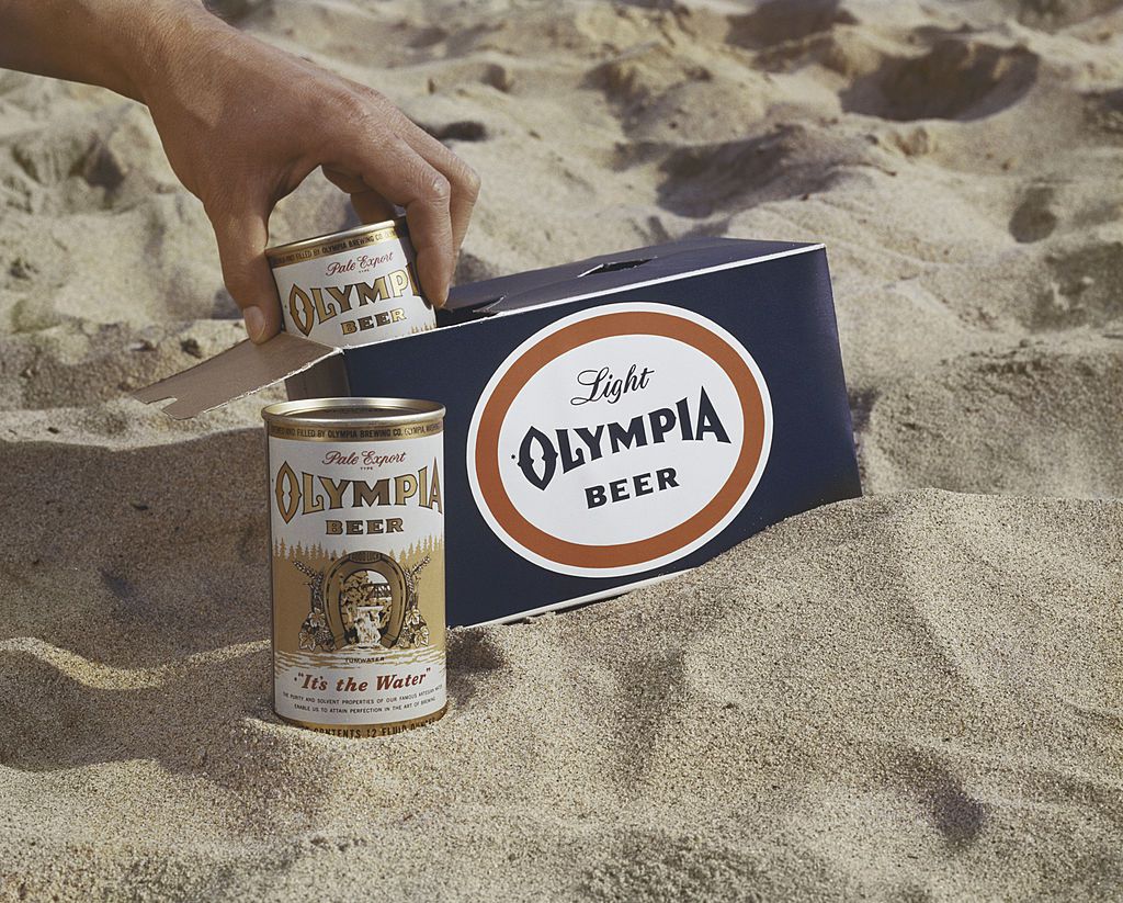 Man holding drinks can with box on sand, close-up