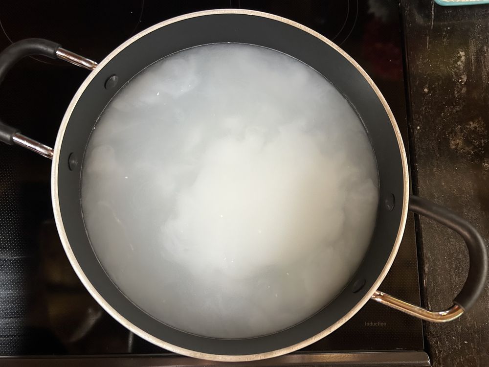 A black pot filled with cloudy, starchy water sits on a stovetop, likely after boiling rice or pasta. The water appears white due to starch released from the cooked food.