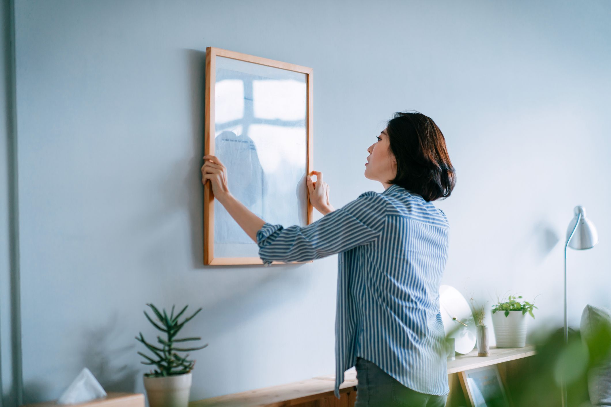 Woman hanging up wall art on a blue wall