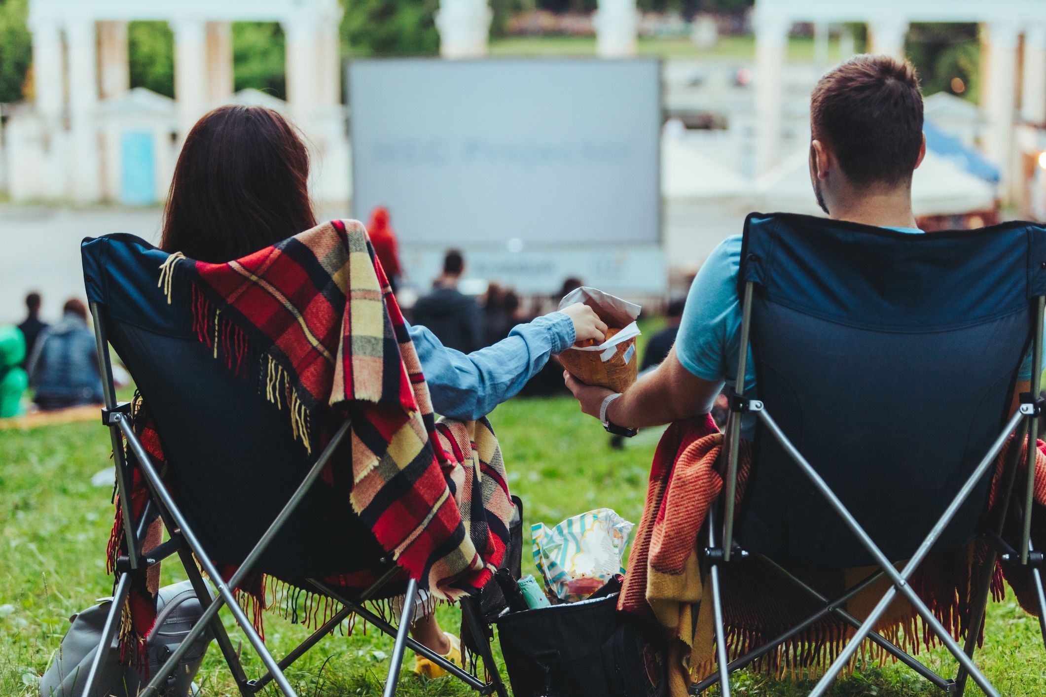 couple sitting in camp-chairs in city park looking movie outdoors at open air cinema lifestyle