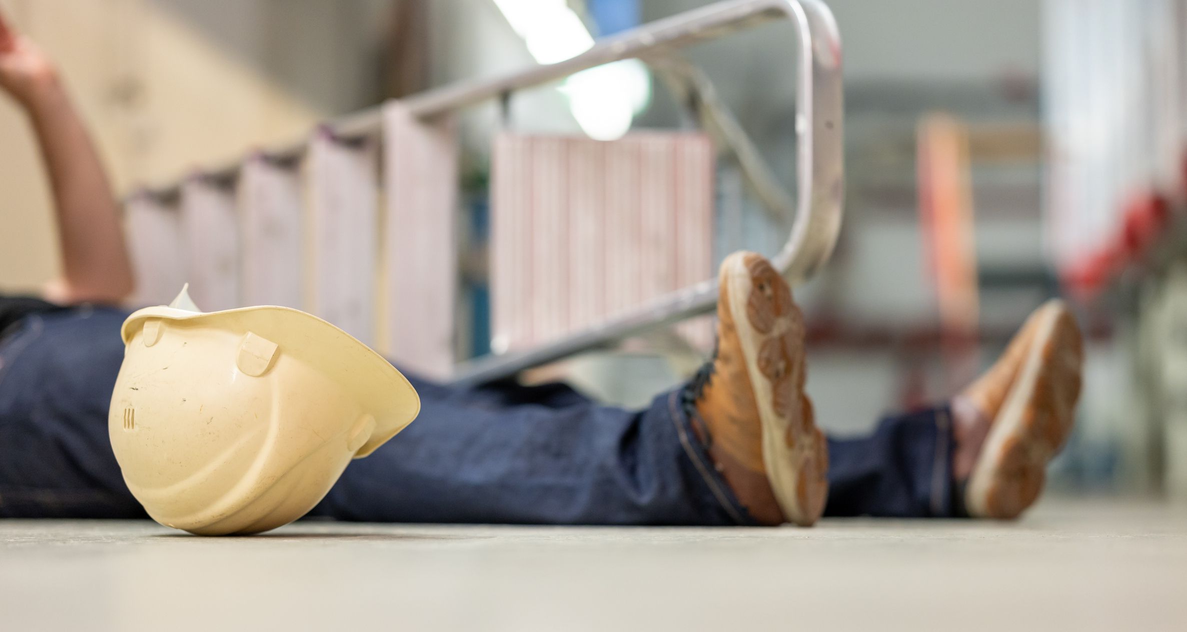Male body lying on the floor after a work accident. Fallen ladder and safety helmet lying next to the body.