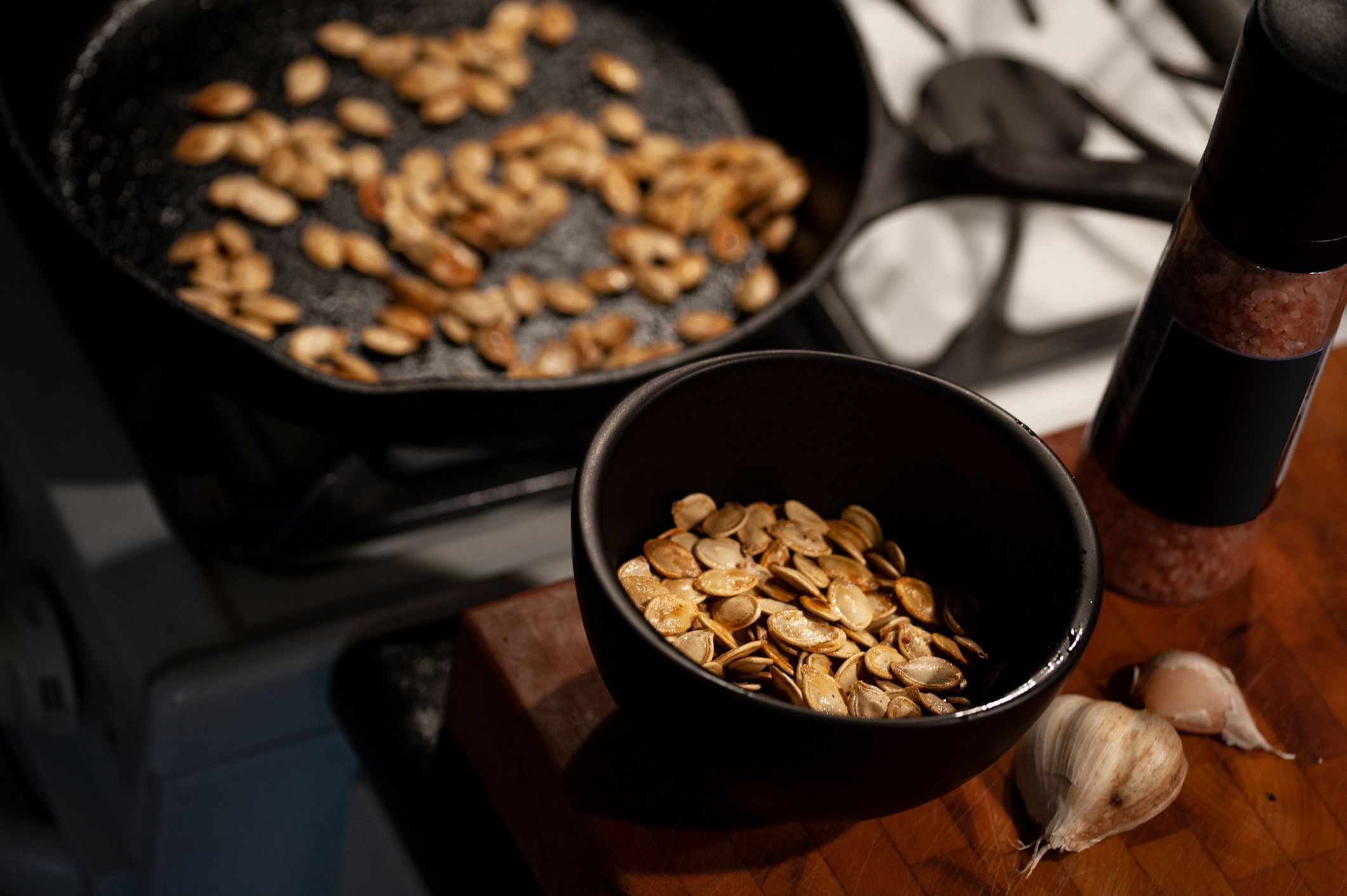 Pan roasted pumpkin seeds with elements of kitchen and cooking ingredients in the background