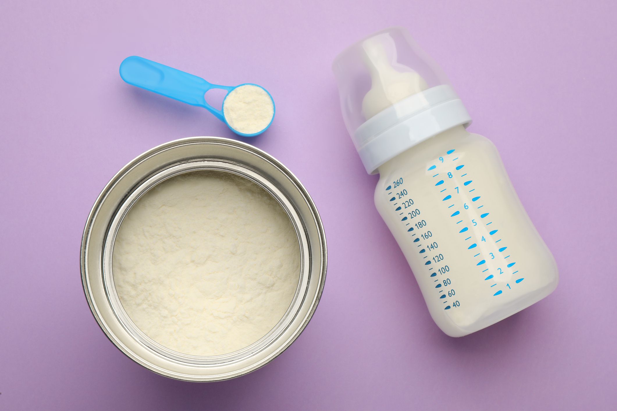 Feeding bottle with infant formula and powder on violet background, flat lay