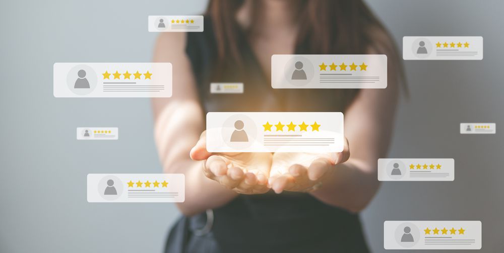 A person holds out their hands with floating digital review icons above them, each showing user profiles and five-star ratings, symbolizing positive feedback and customer satisfaction.