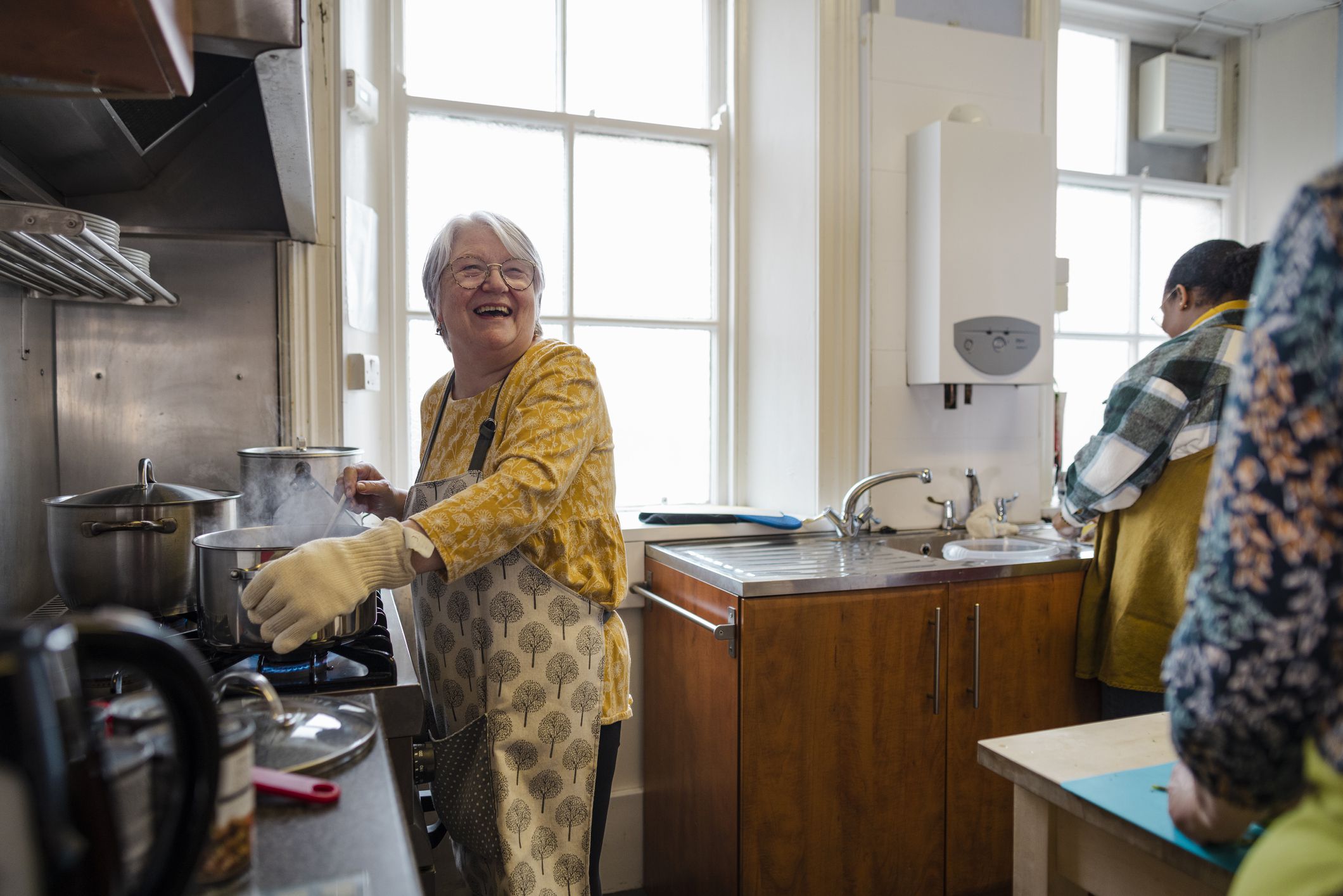 A shot of volunteers cooking in the kitchen at a warm hub/food bank which is a safe place for people to enjoy a warm and friendly environment in the community with the current cost of living increasing. They are making roast dinners for the visitors.