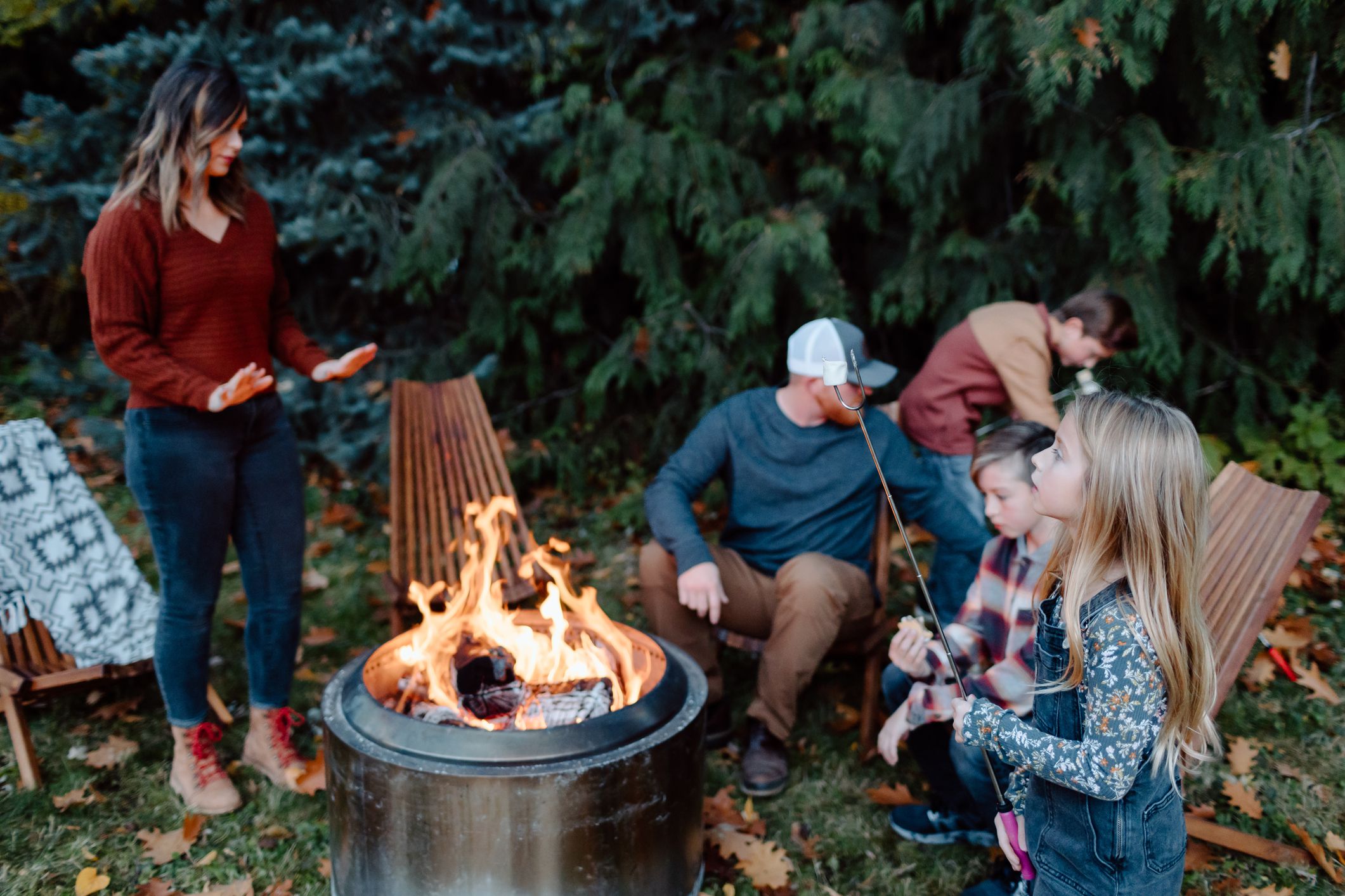 A family with elementary age children gathers around a fire pit in the backyard and roasts marshmallows.