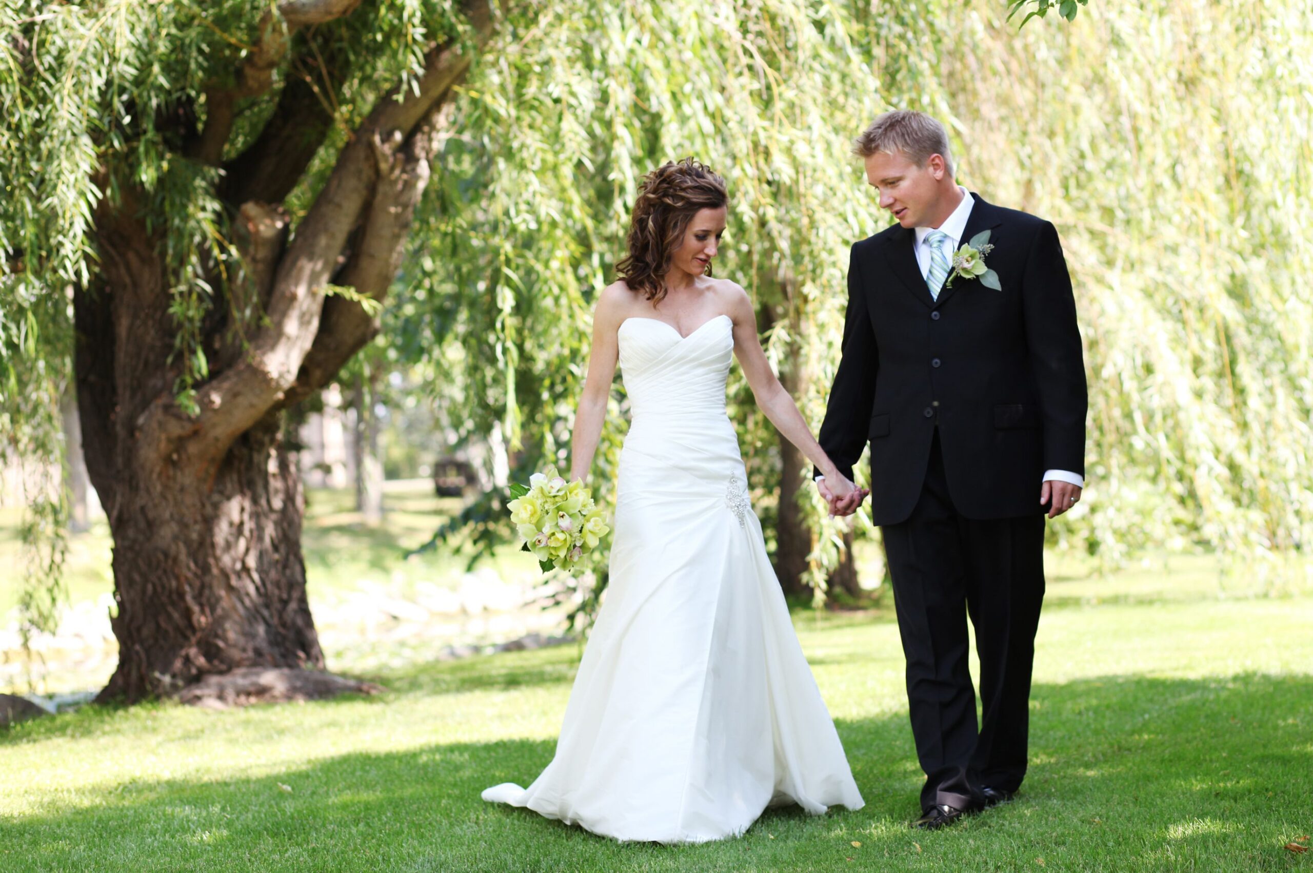Bride and Groom holding hands, walking near a willow tree