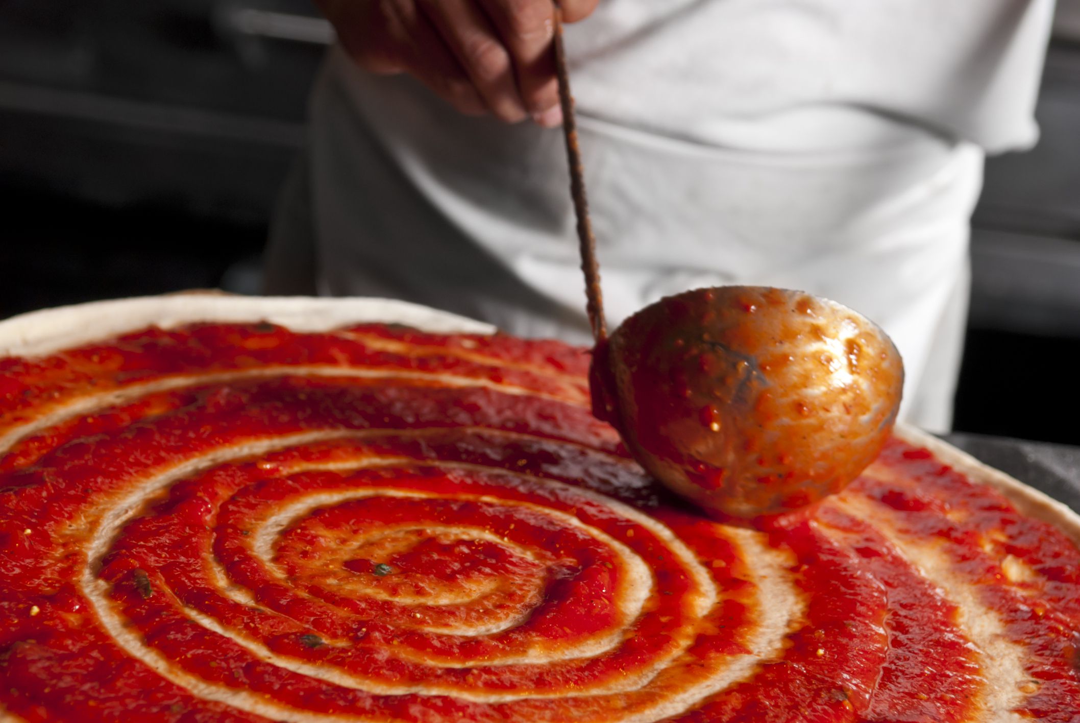Selective-focus image of chef using ladle to spread sauce on a pizza