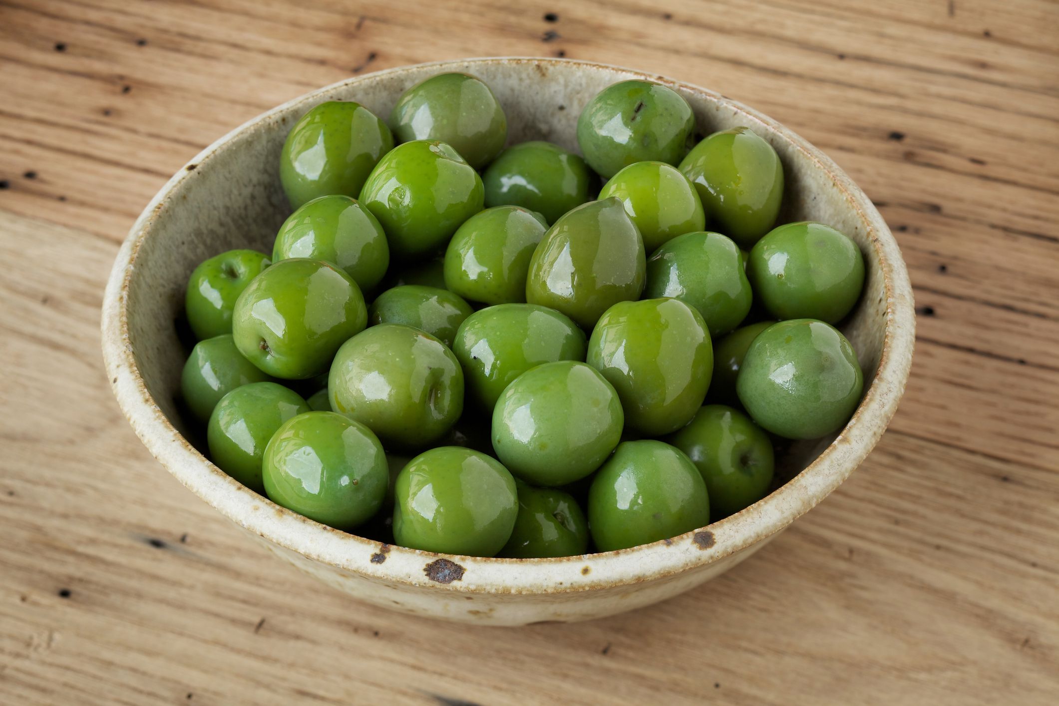 Natural light photo of small bowl of Castelvetrano Sicilian green olives on rustic wood backgroundPlease view more rustic food images here:
