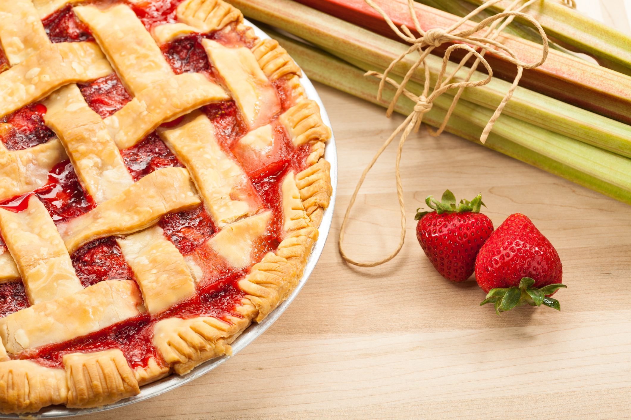 Homemade strawberry rhubarb pie with Strawberries and rhubarb on a wooden cutting board. Traditional late summer/early fall dessert.