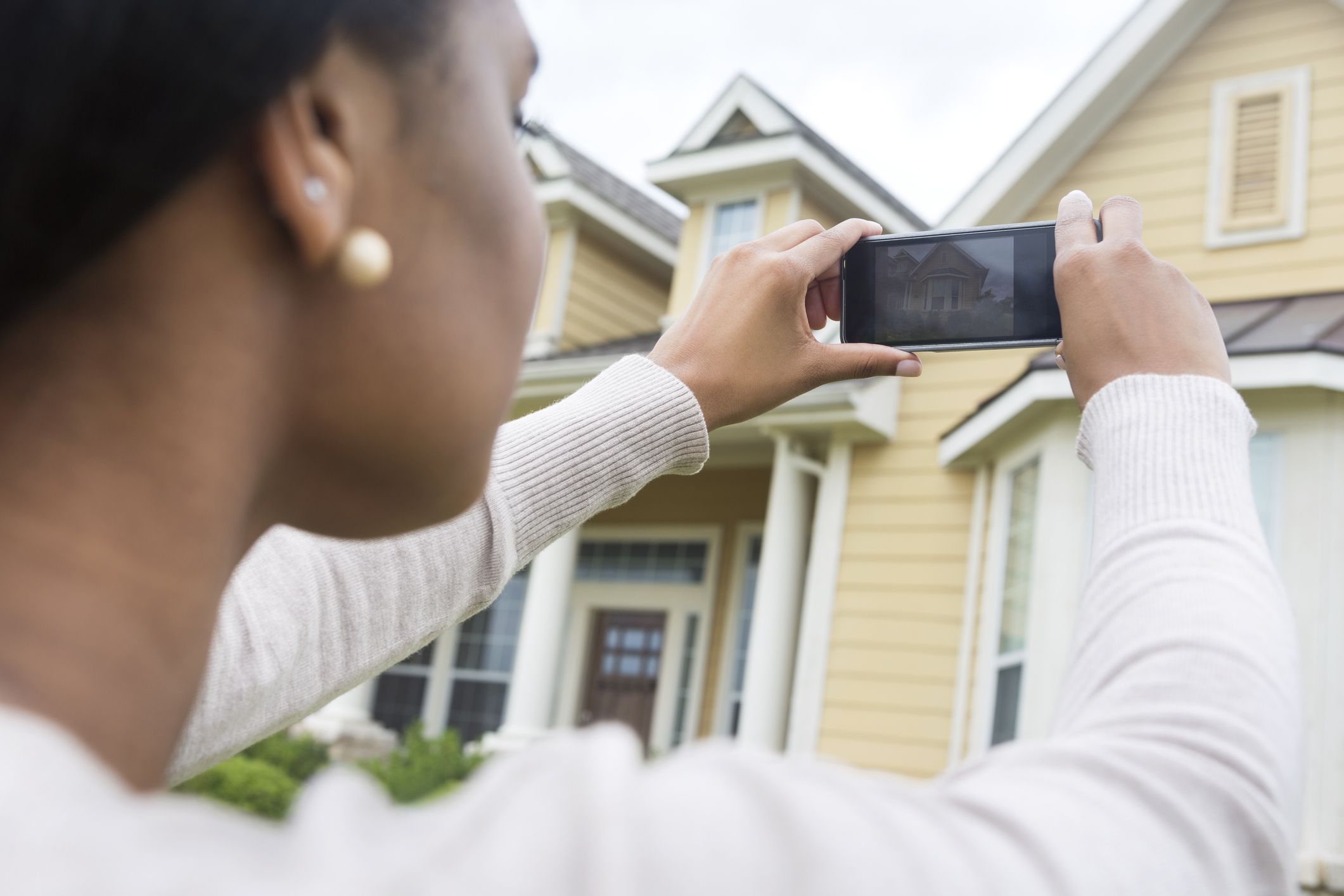 Young woman taking photo of new home with smart phone