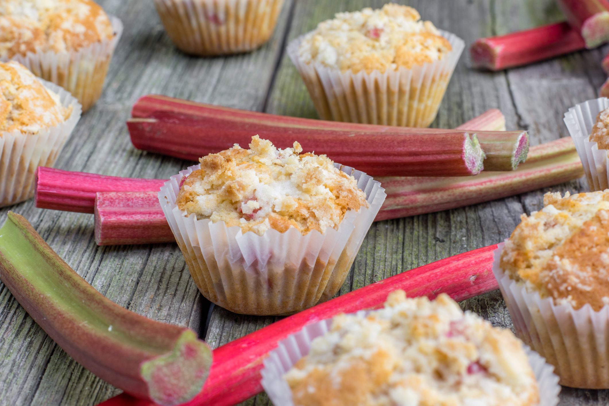 Rhubarb muffin in paper cups with rhubarb petioles in the background on Old Wooden Board