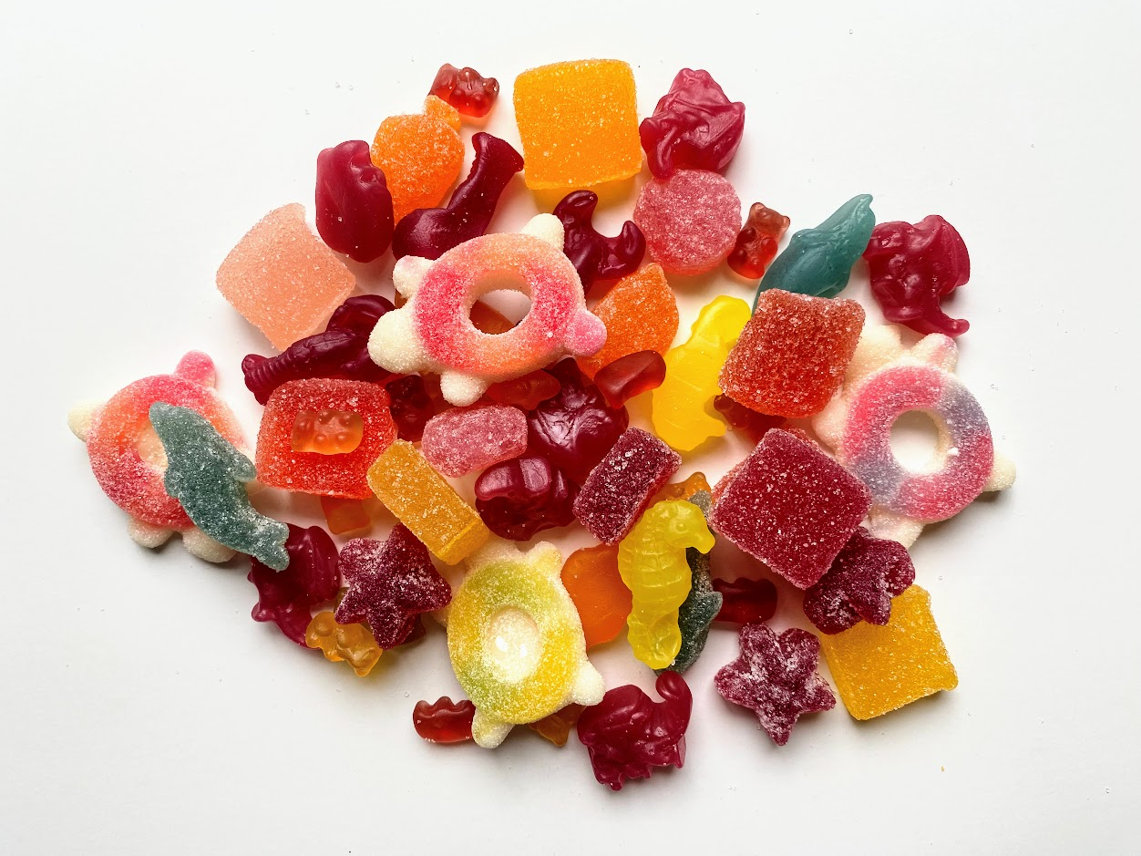 A pile of assorted colorful gummy candies in various shapes, including rings, animals, and squares, scattered on a white background.