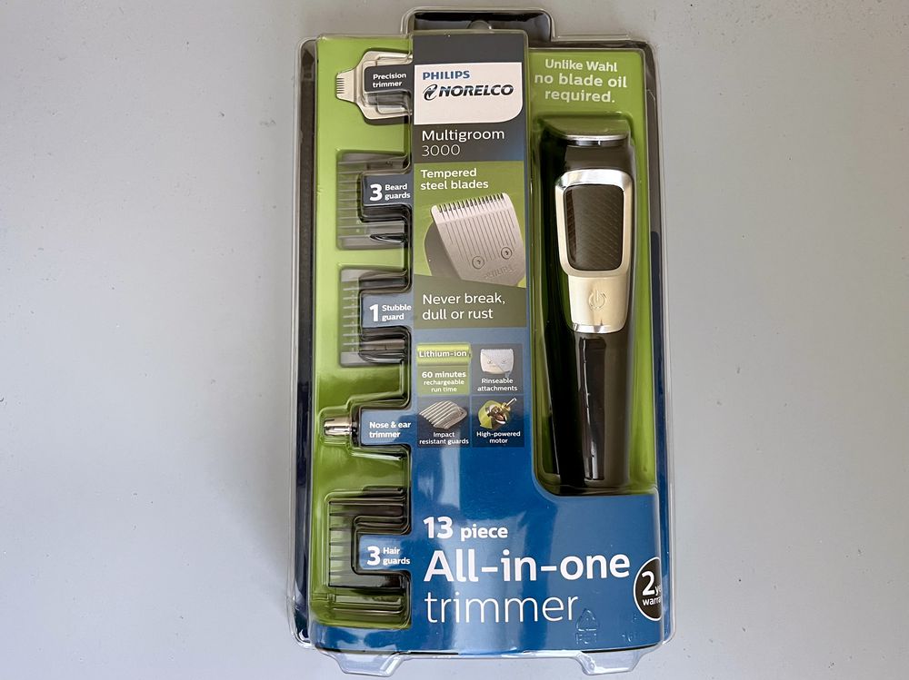 Philips Norelco Multigroom 3000 in packaging, showing trimmer, 3 beard guards, and 2 hair guards. Text highlights tempered steel blades, no blade oil needed, and 13-piece all-in-one grooming kit.