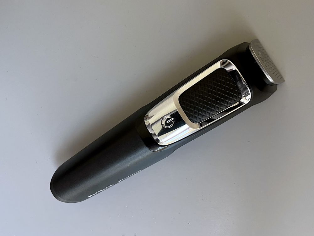 A black and silver electric trimmer with a textured grip and a power button is placed on a light gray surface.