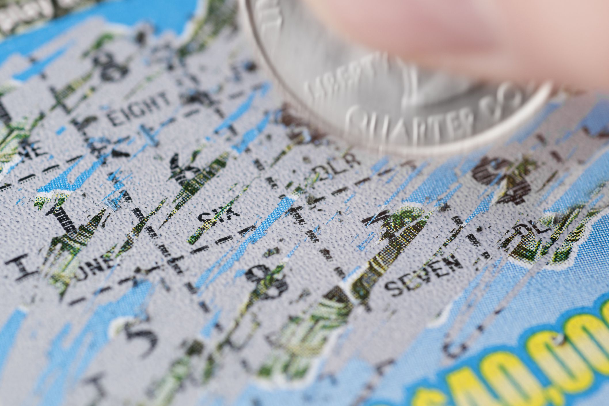 Closeup of quarter in motion scratching off a scratch-off lottery ticket revealing numbers