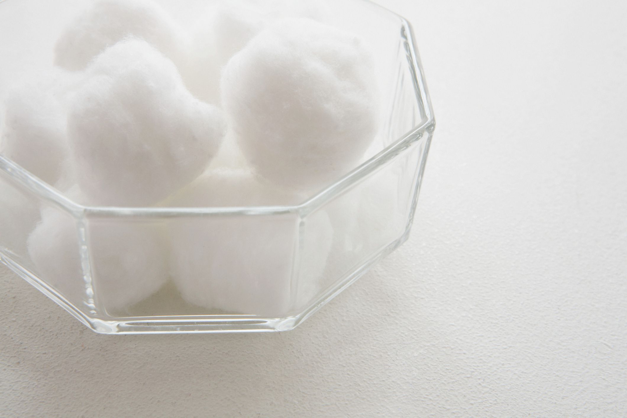 A glass bowl filled with cotton balls against a white background