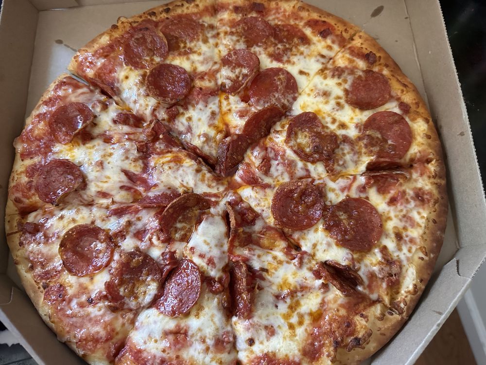 A freshly baked pepperoni pizza in a cardboard box, sliced into eight pieces with melted cheese and evenly spaced pepperoni slices on a golden crust.