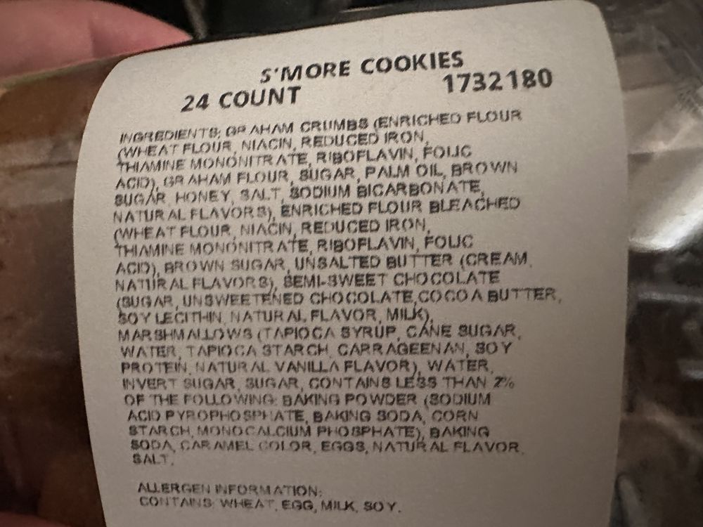 A close-up of a label for S'more Cookies, listing ingredients such as graham crumbs, flour, sugar, butter, chocolate, eggs, and flavorings, along with allergen information for wheat, egg, milk, and soy.