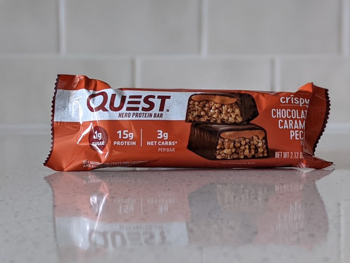 Quest Hero Protein Bar, Crispy Chocolate Carmel Pecan, on a light grey countertop with light grey tiles in the background
