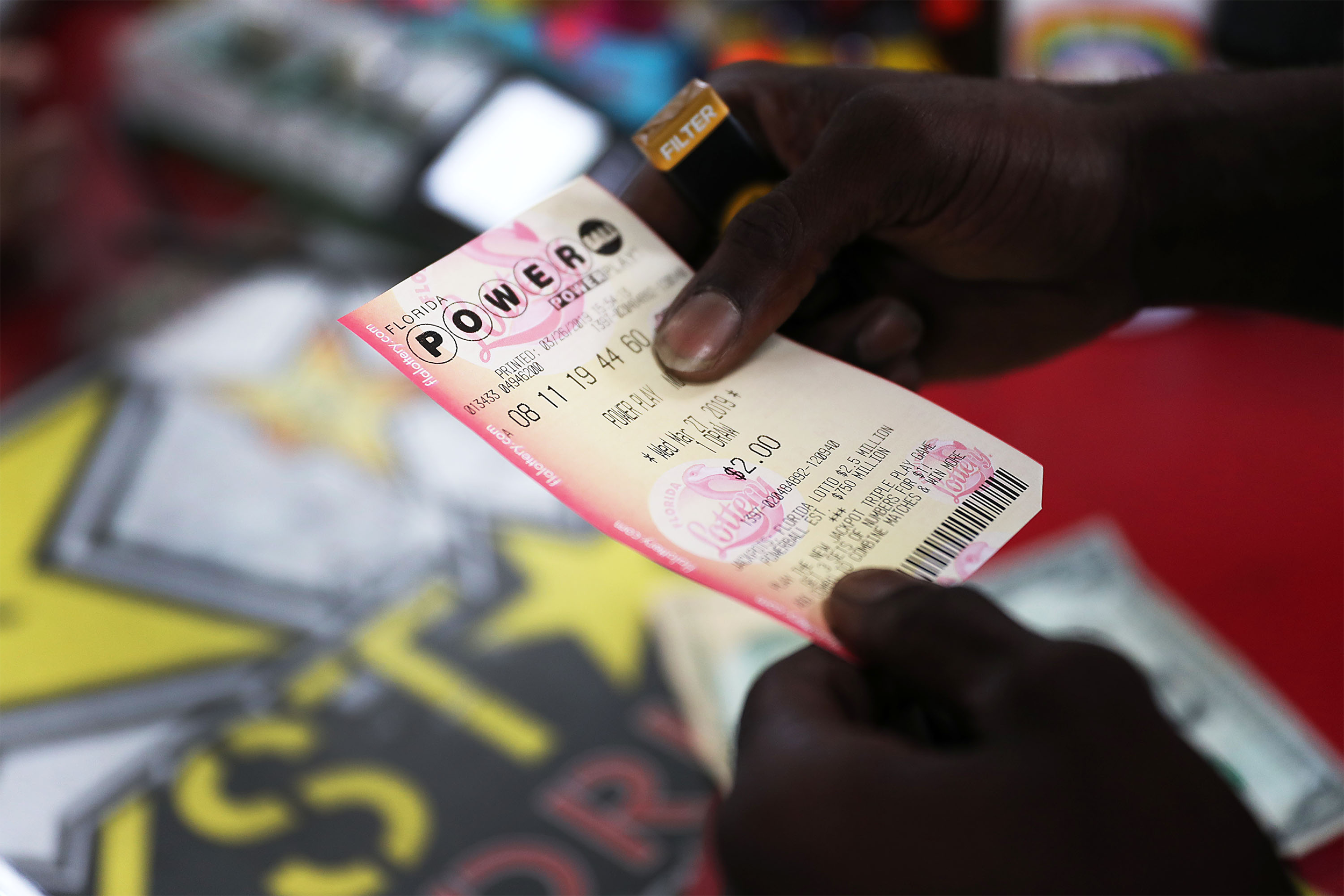 Two hands hold a Powerball ticket with one set of numbers, selective focus, cash register and counter blurred in the background