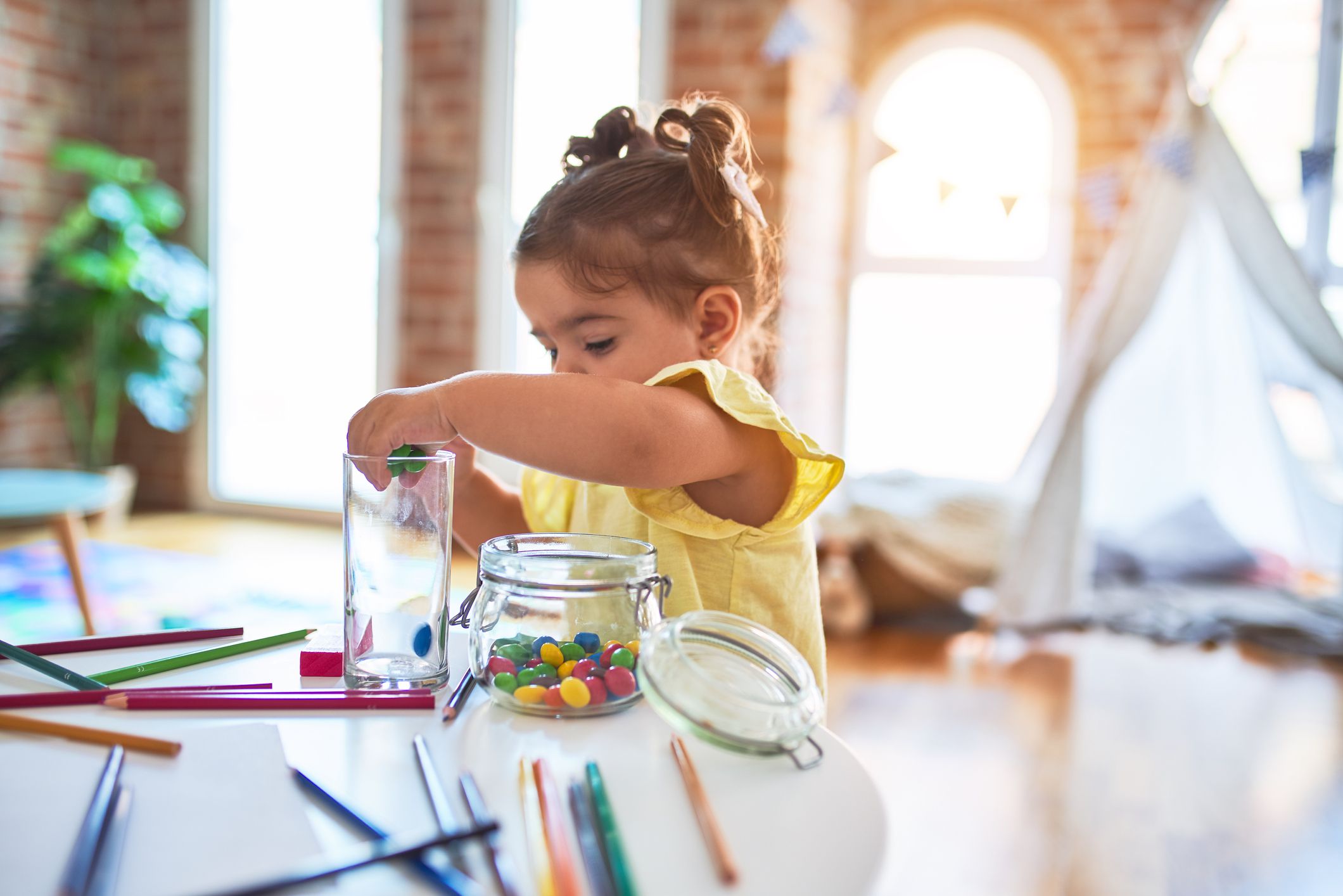 Beautiful toddler standing playing with chocolate colored balls on the table at kindergarten