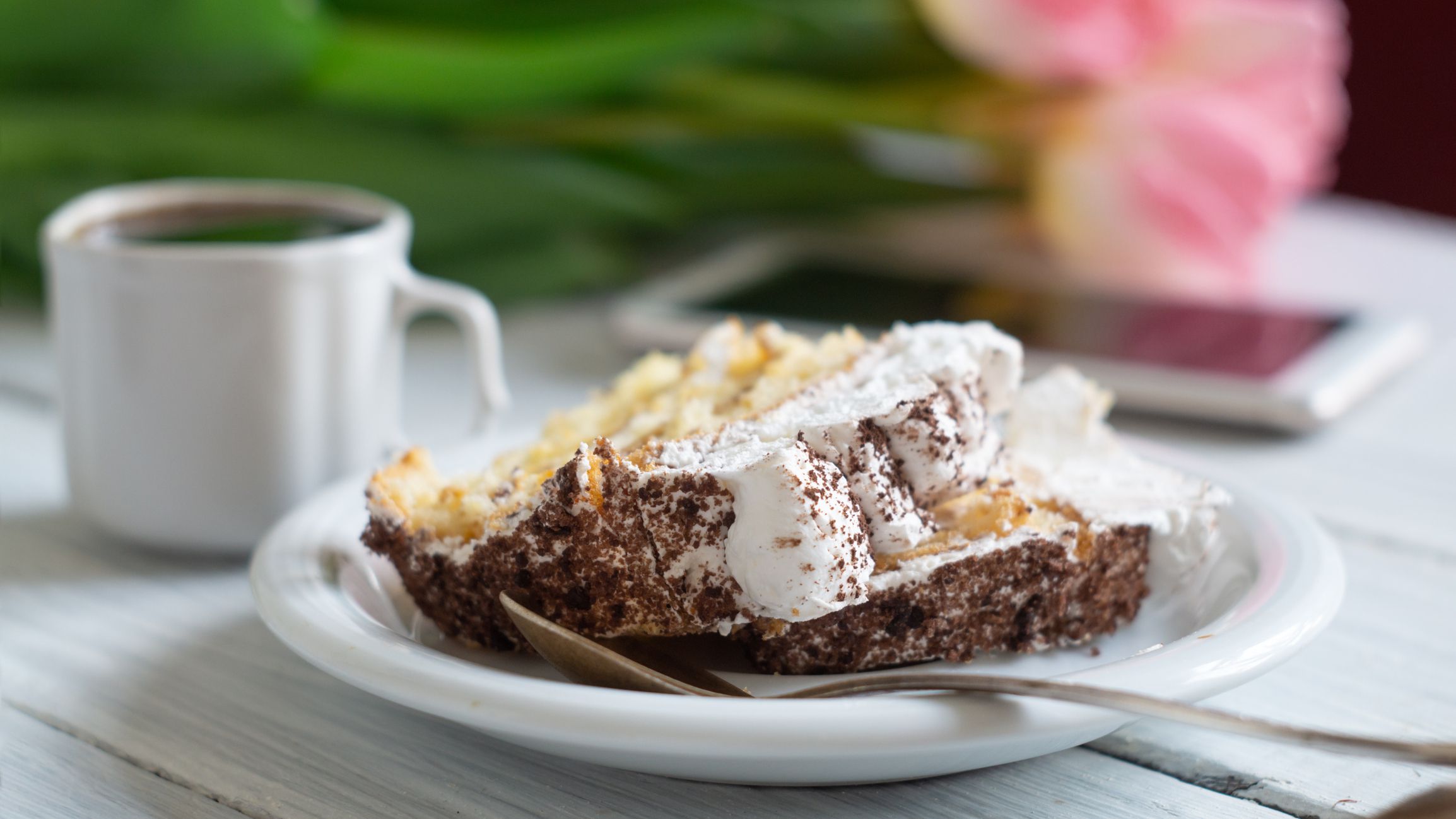 Tiramisu cake, pink tulips and a cup of coffee on a white wooden table