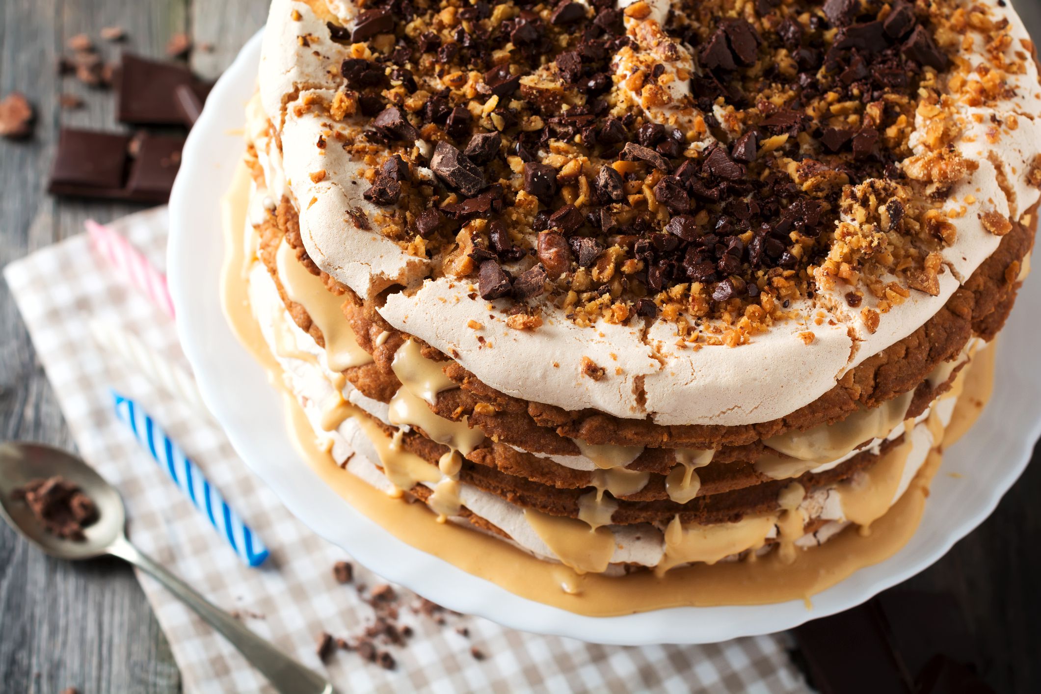 Homemade layered pastry cake and meringue, walnuts, dark chocolate on old wooden background. Selective focus.