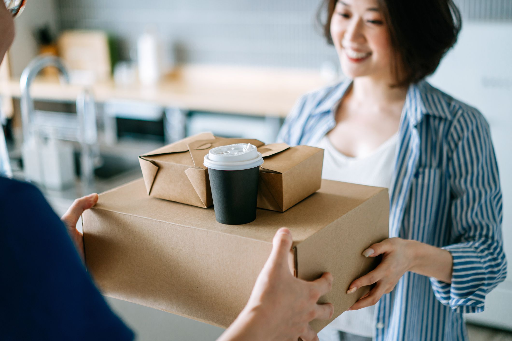 Close up of beautiful and cheerful young Asian woman receiving home delivery takeaway food order from a delivery man at home. Eating at home concept