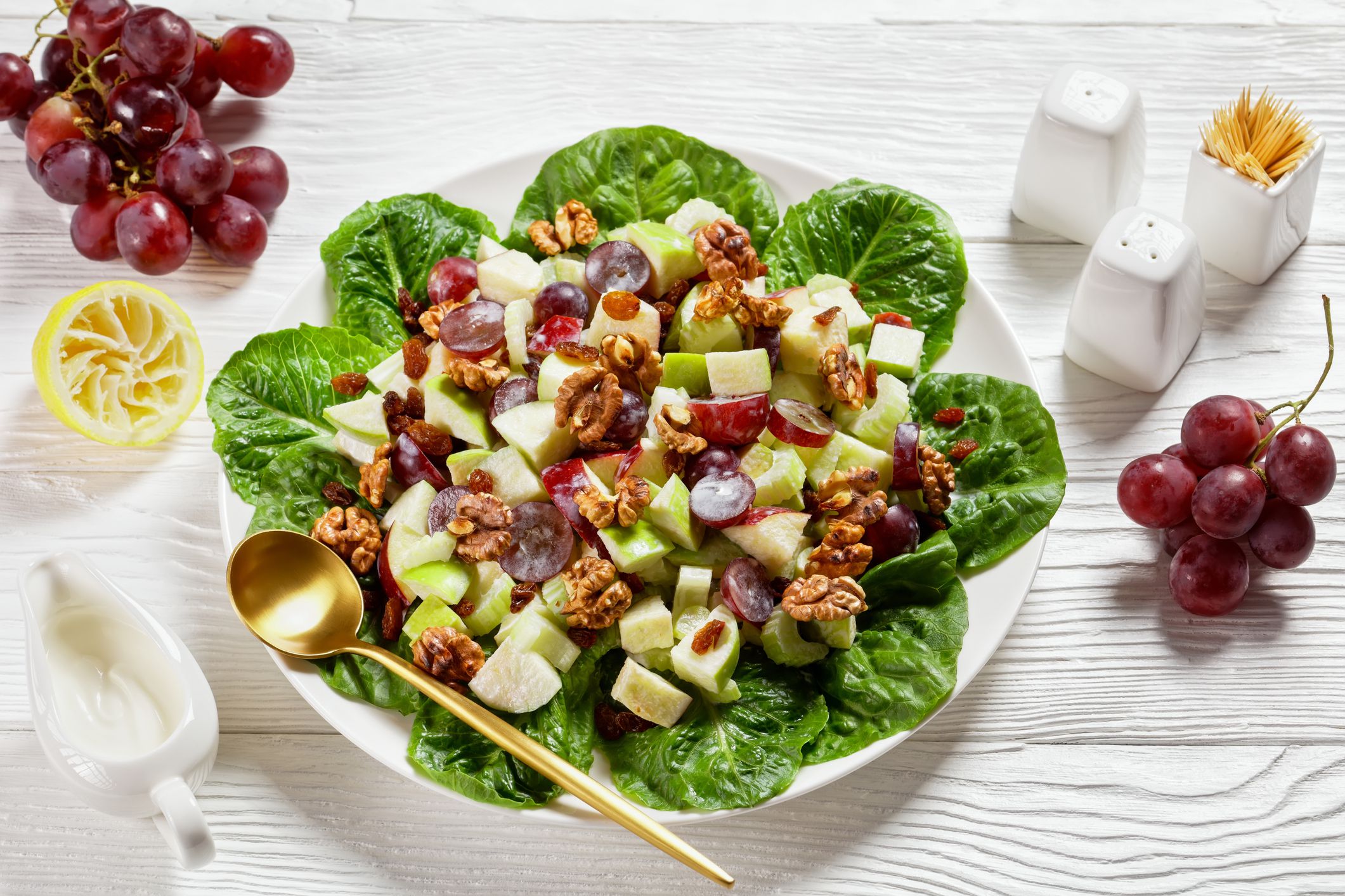 Waldorf salad with red grapes, celery, fresh green apple, walnuts, raisins on a pad of fresh lettuce leaves on a white plate on a wooden table,american cuisine