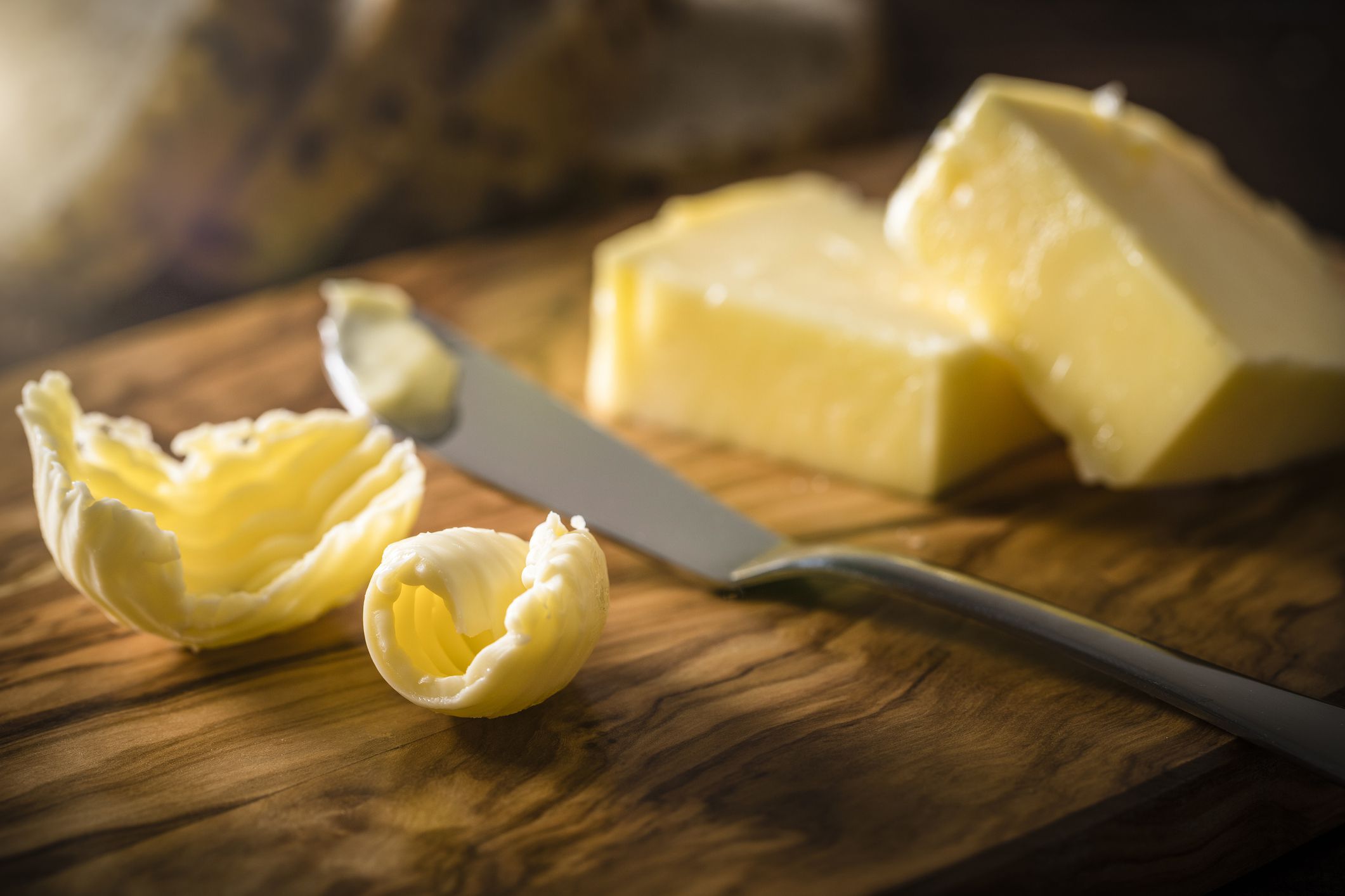 Front view of a cutting board with two butter curls and a butter knife on top.