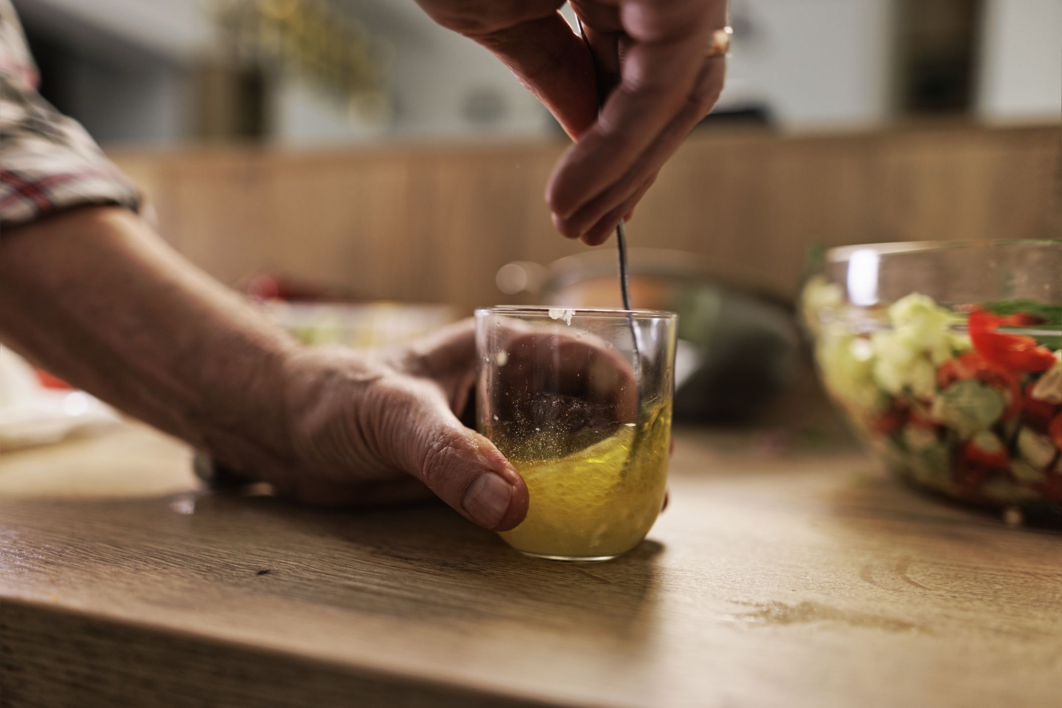 Senior couple is preparing a healthy vegetable salad at home. They are preparing the vinaigrette dressing. The man is mixing lemon juice with olive oil and garlic.Canon R5