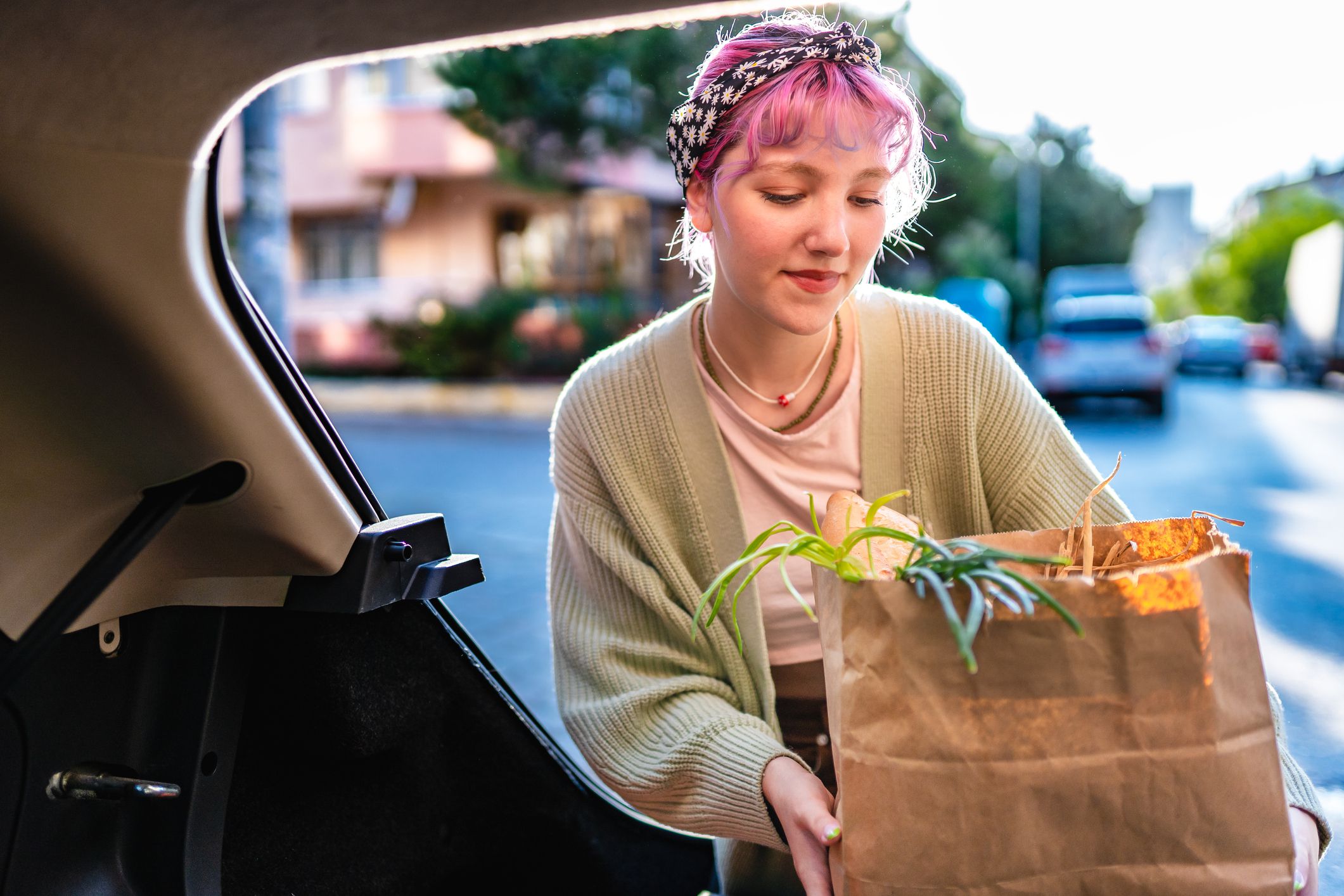 Young woman with colored hair puts her grocery shopping in the trunk of her car