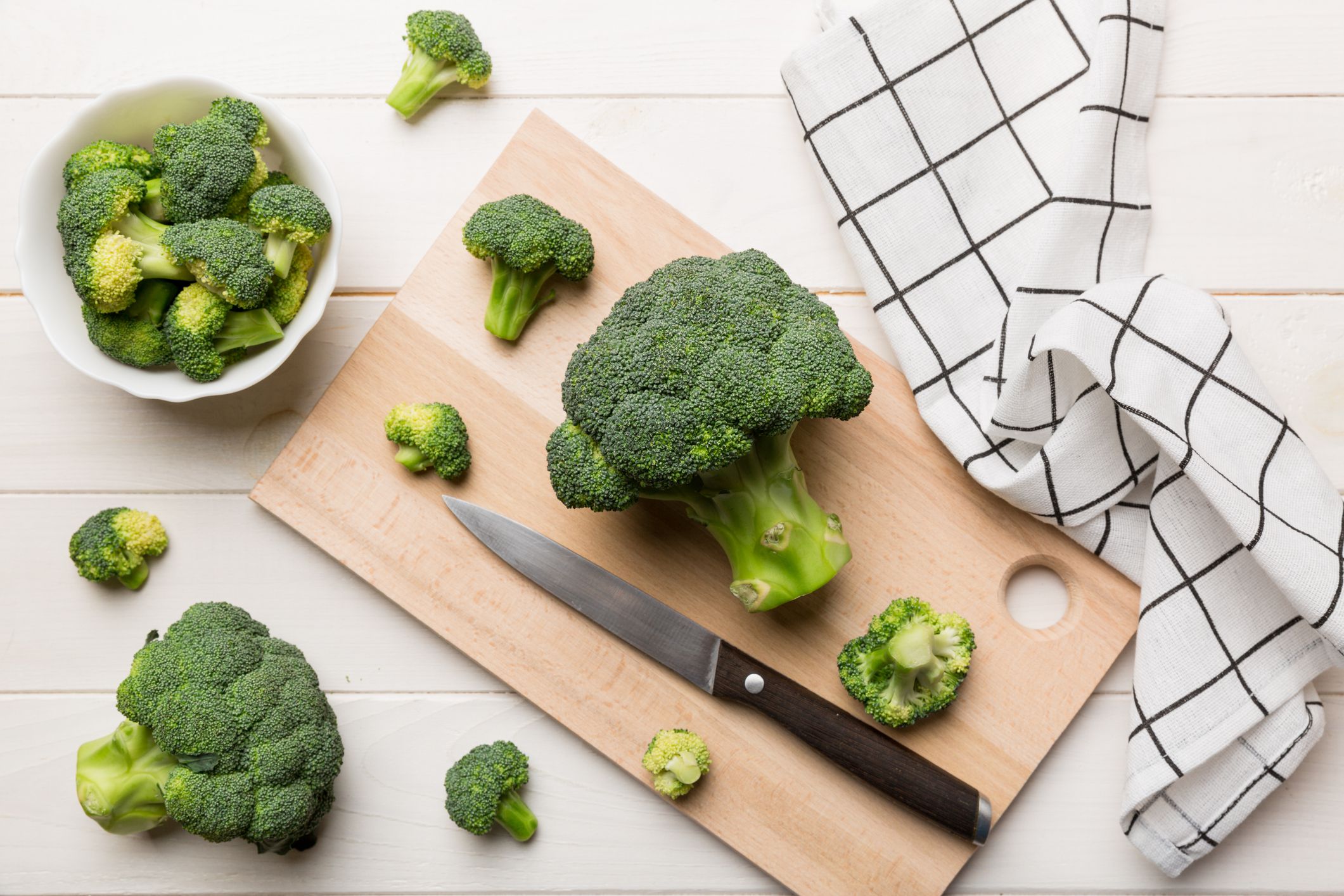 fresh green broccoli on wooden cutting board with knife. Broccoli cabbage leaves. light background. Flat lay.